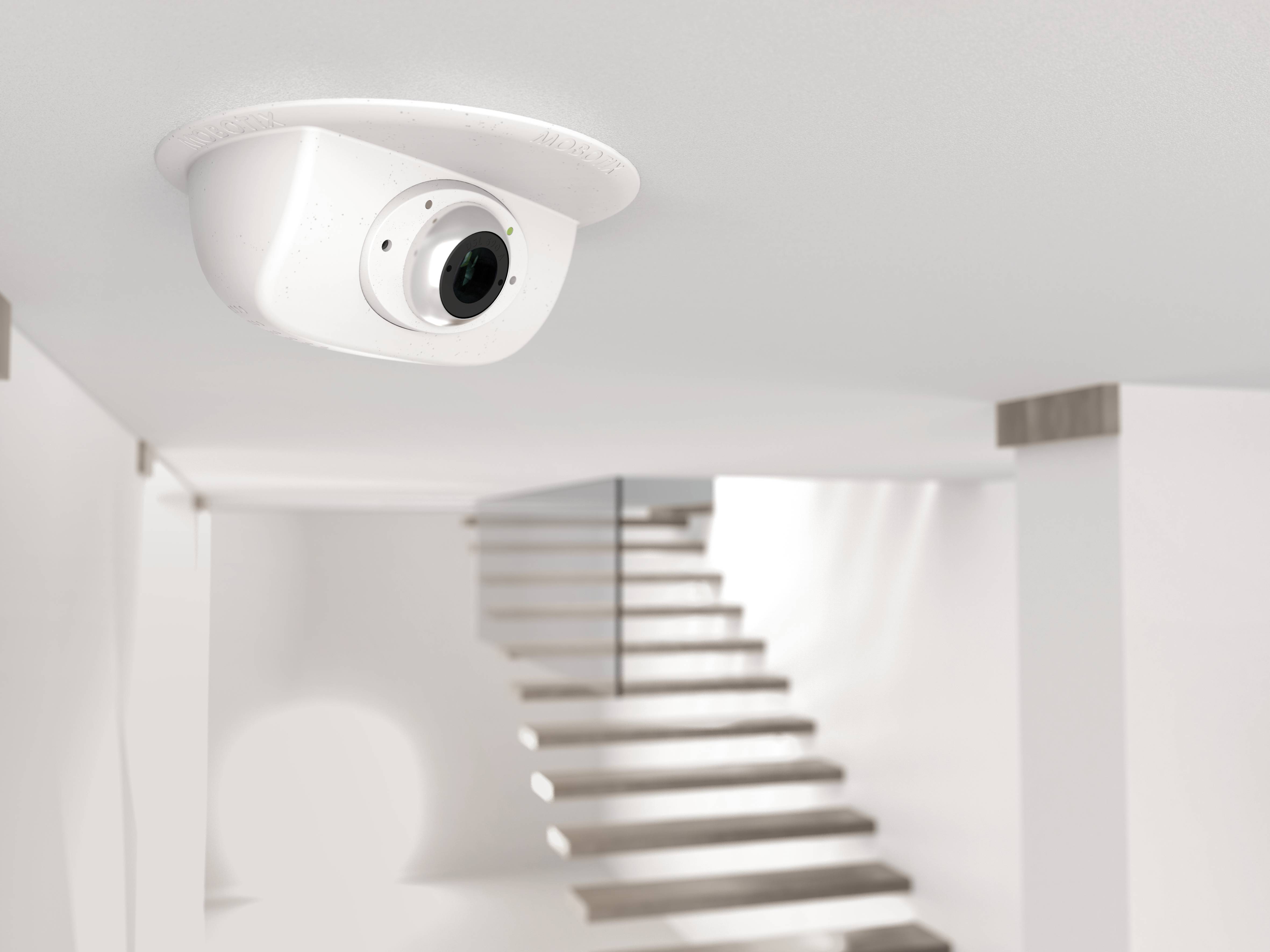 Telecamera di sorveglianza sul soffitto di un corridoio moderno e luminoso con una scala sullo sfondo.