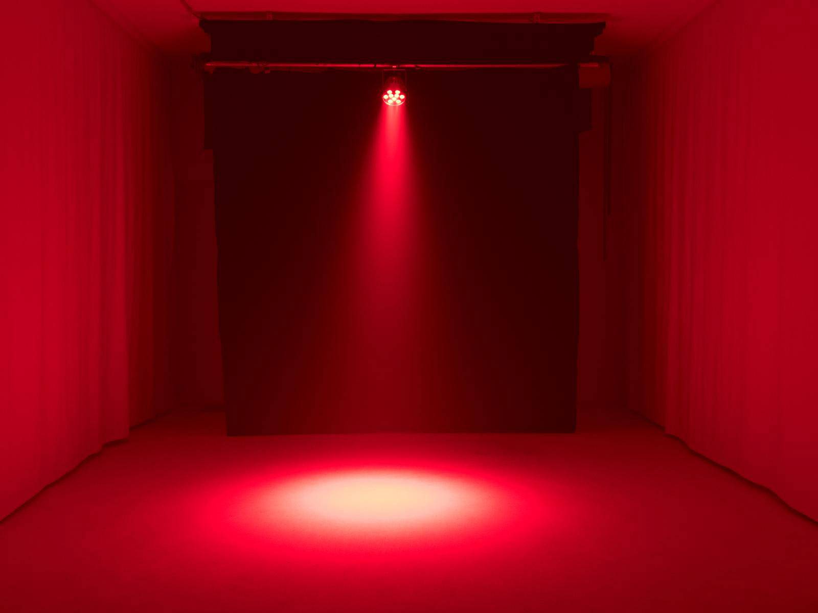 Uno spazio vuoto con un raggio di luce rossa diretto verso il pavimento. Lo sfondo è scuro.