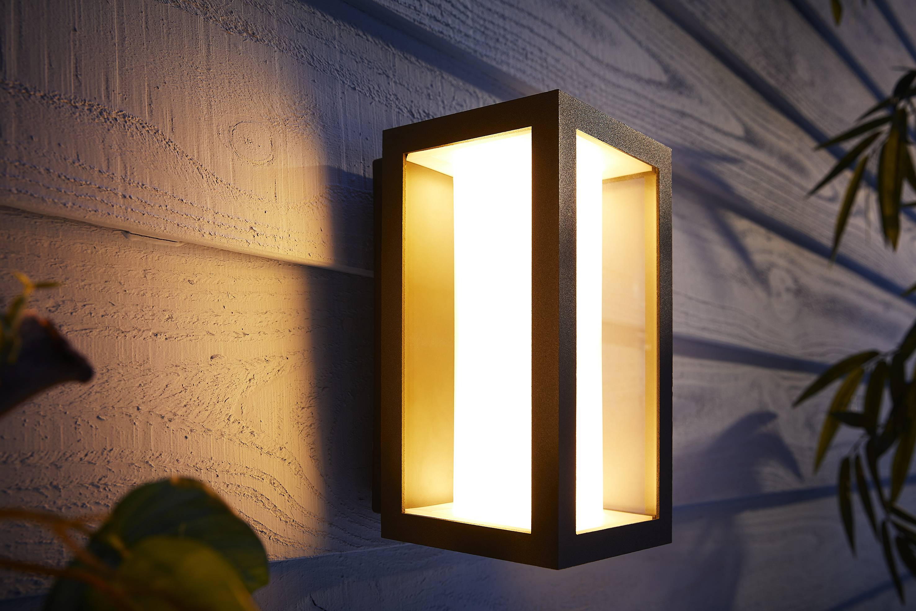 Applique da esterno su una facciata in legno che emana una luce calda, creando un'atmosfera serale accogliente.