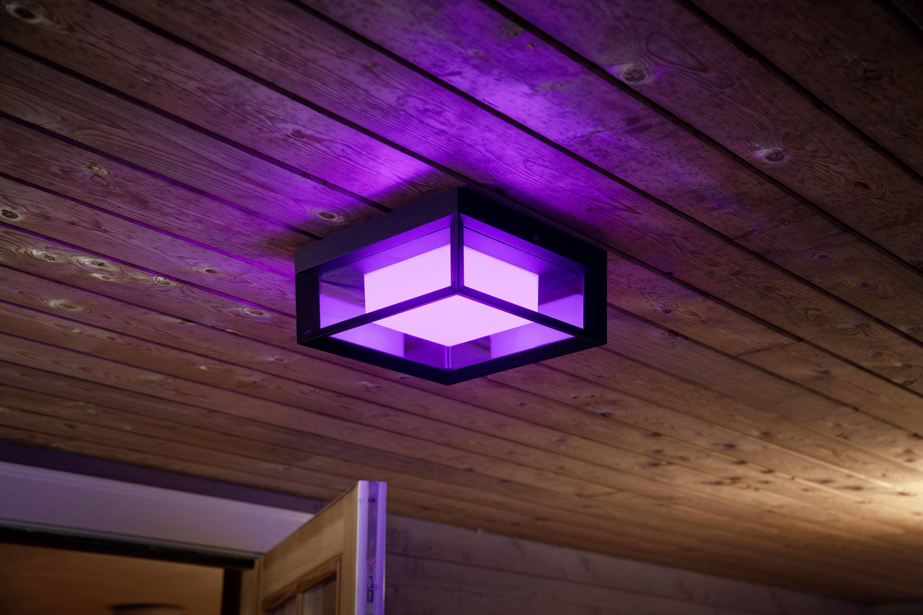 Un lampadario moderno con illuminazione viola è montato su un soffitto in legno. La lampada emana una luce soffusa.