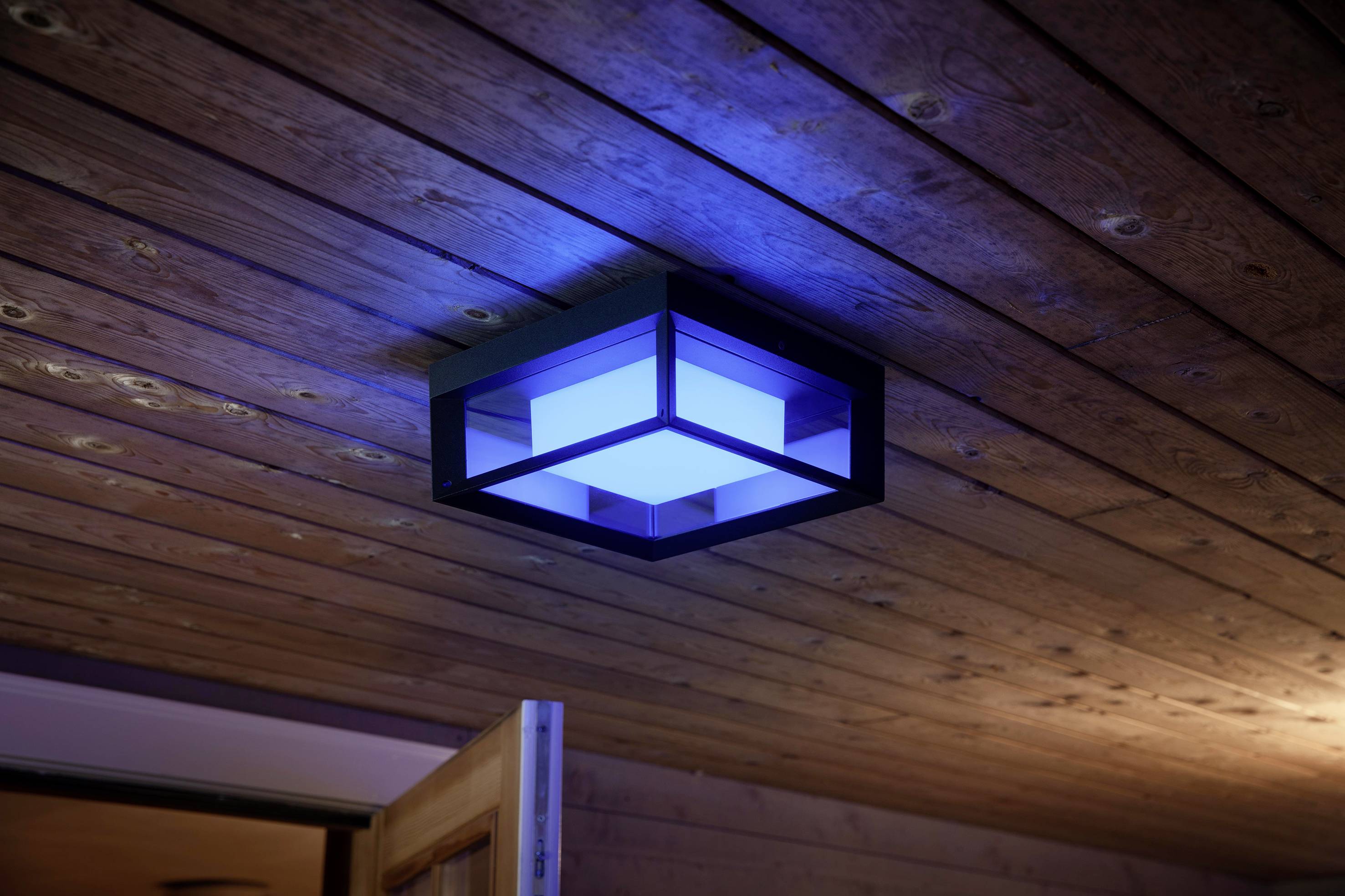 Lampada da soffitto con illuminazione blu e design moderno montata su un soffitto in legno. Porta parzialmente aperta in primo piano.