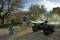 'Un uomo sta pulendo un ATV con un idropulitrice in un cortile. Alberi e un edificio sono visibili sullo sfondo.'