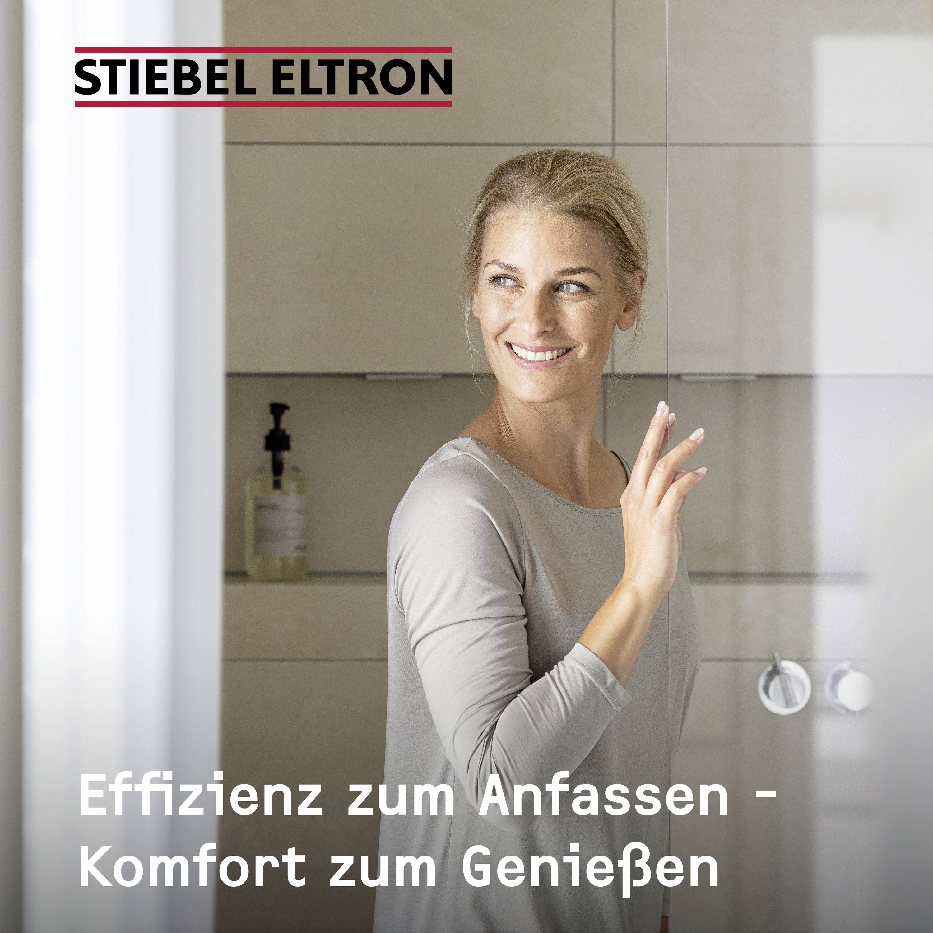 Una donna sorridente tocca una superficie di vetro, accanto il testo 'Efficienza da toccare - Comfort da gustare'. Sullo sfondo il logo di Stiebel Eltron.
