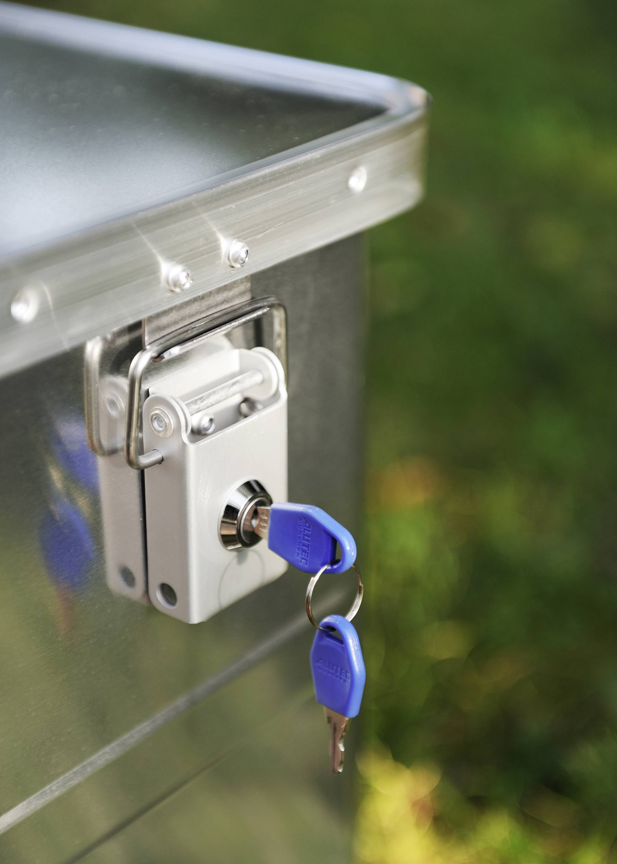 Un lucchetto d'argento con due chiavi blu che pendono dal lucchetto, fissato a un armadietto metallico.