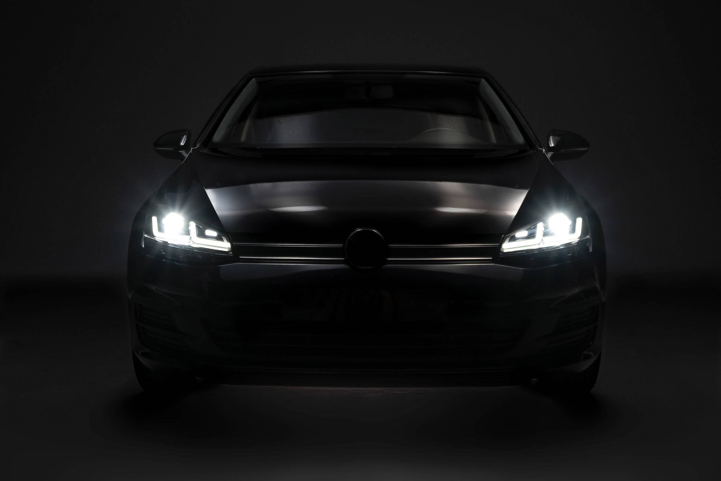 Un'auto risplende nell'oscurità con i fari accesi. Visuale frontale sulla vettura nera che evidenzia i suoi fari.