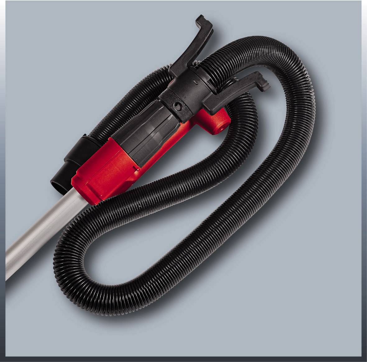 Un tubo dell'aspirapolvere rosso e nero con un lungo tubo flessibile è posizionato su uno sfondo grigio.
