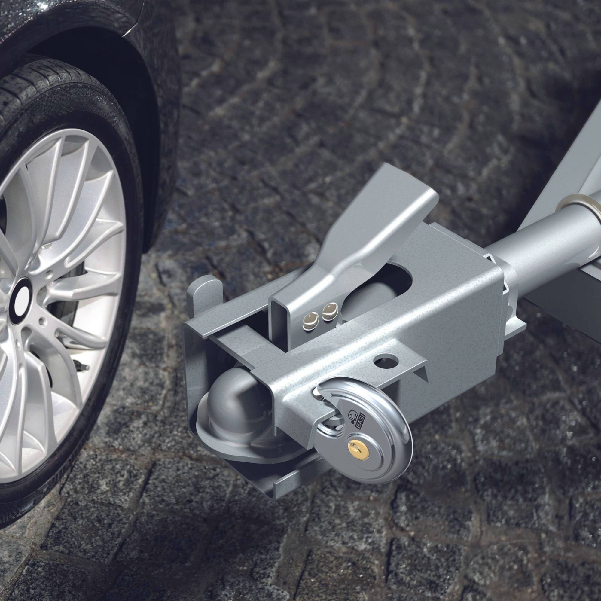 Primo piano di un rimorchio agganciato al gancio di traino di un'auto ferma su un lastricato di ciottoli.