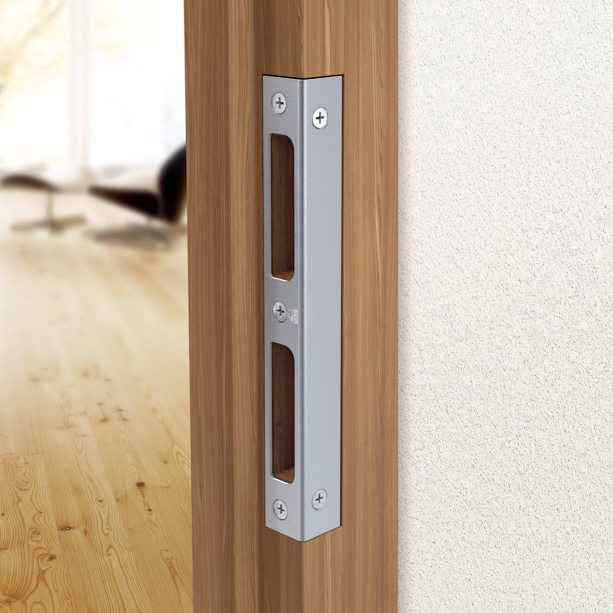 Una placca di impatto in metallo è montata sul bordo di uno stipite di porta in legno, che consente a un bullone di chiusura di assicurare la porta, con una stanza sfocata sullo sfondo.
