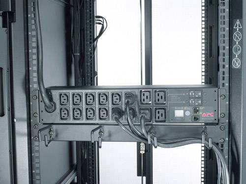 'Barra di distribuzione elettrica in un rack server con multiple prese, cavi e un display digitale. Logo APC in basso a destra.'