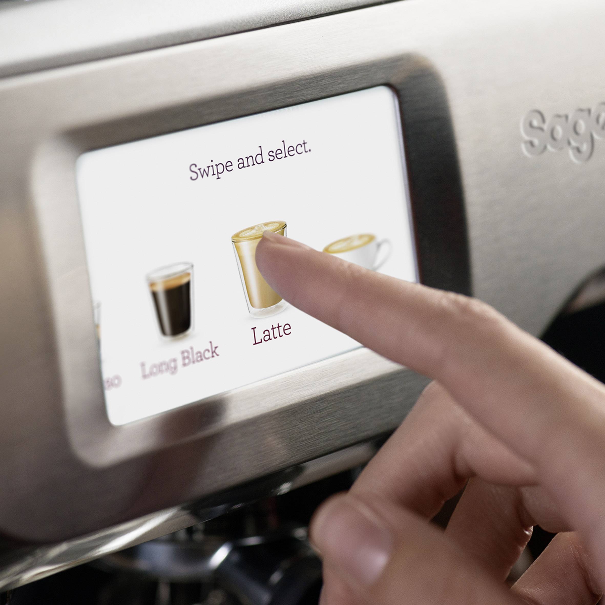 Un dito tocca lo schermo di una macchina da caffè e seleziona l'opzione 'Latte'.