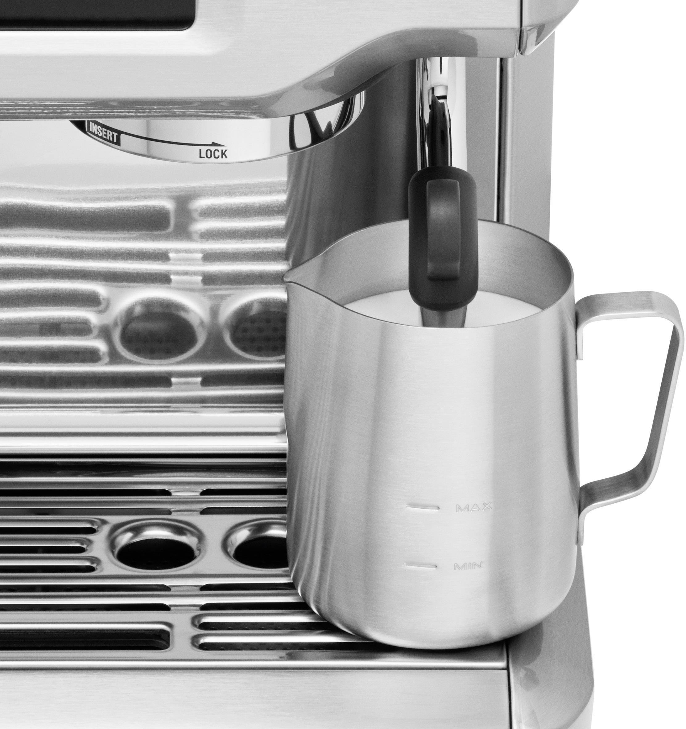 Una brocca di latte viene montata sotto un'erogatore di vapore di una macchina da espresso. La macchina ha un design argentato e moderno.