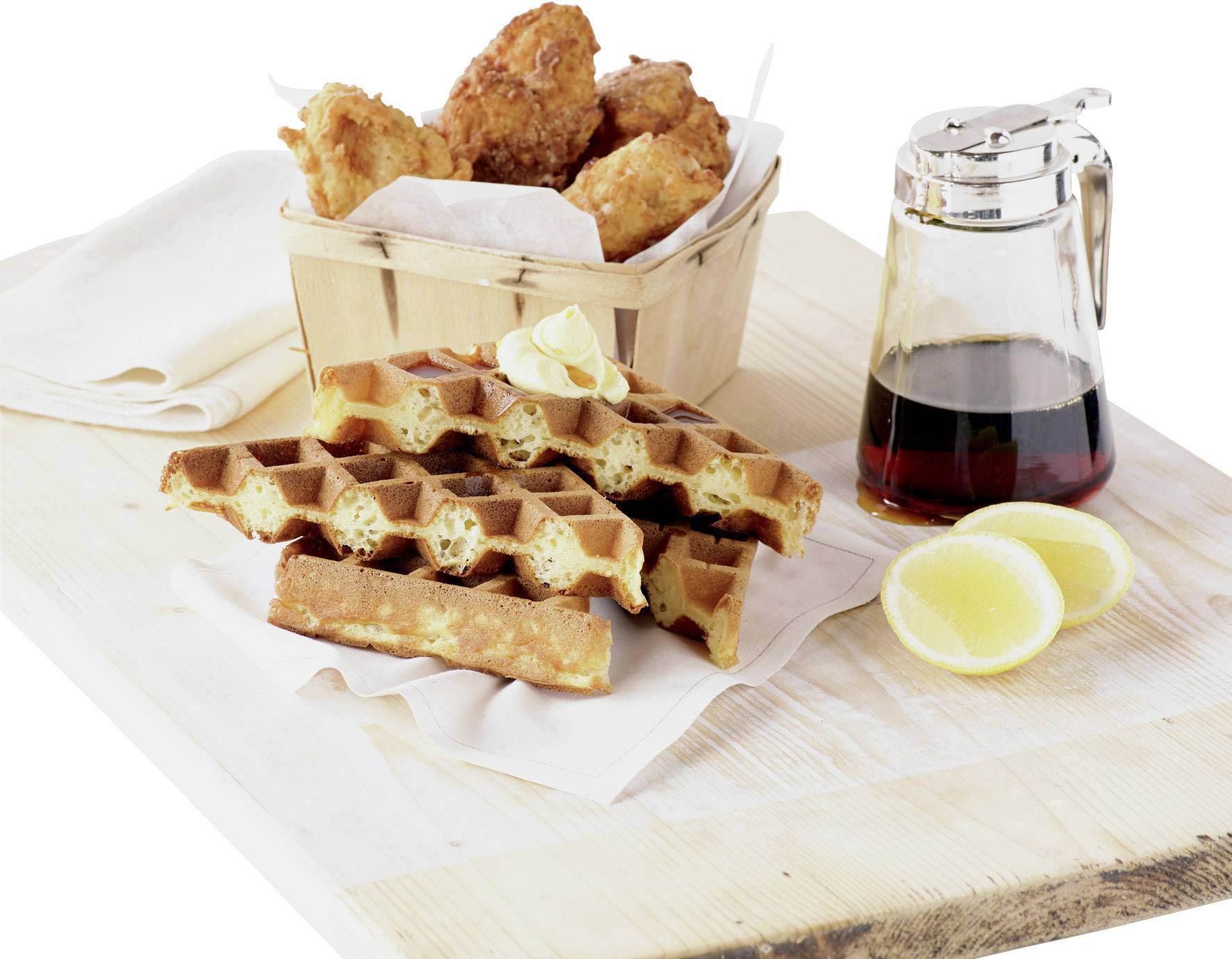 Waffle con burro e fette di limone accanto a sciroppo d'acero e una scatola di pollo fritto su un tagliere.