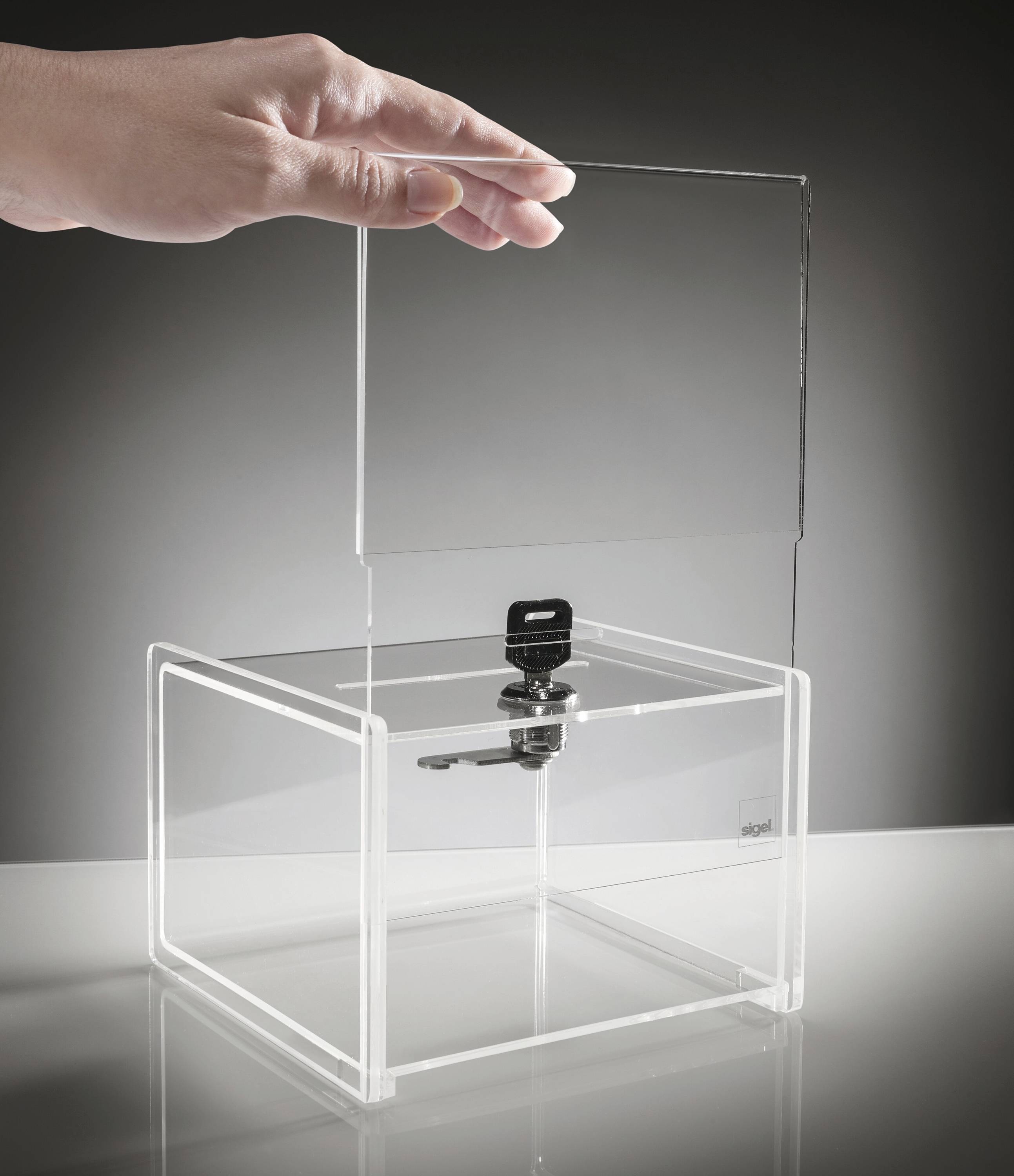 Una mano posiziona un coperchio trasparente in acrilico su una scatola trasparente con un lucchetto, suggerendo sicurezza o protezione del contenuto.