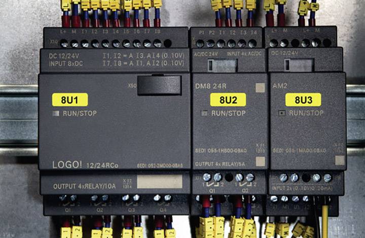 Una serie di quattro dispositivi elettrici di controllo su una piastra metallica, etichettati con '8U1', '8U2', '8U3', circondati da cavi colorati.