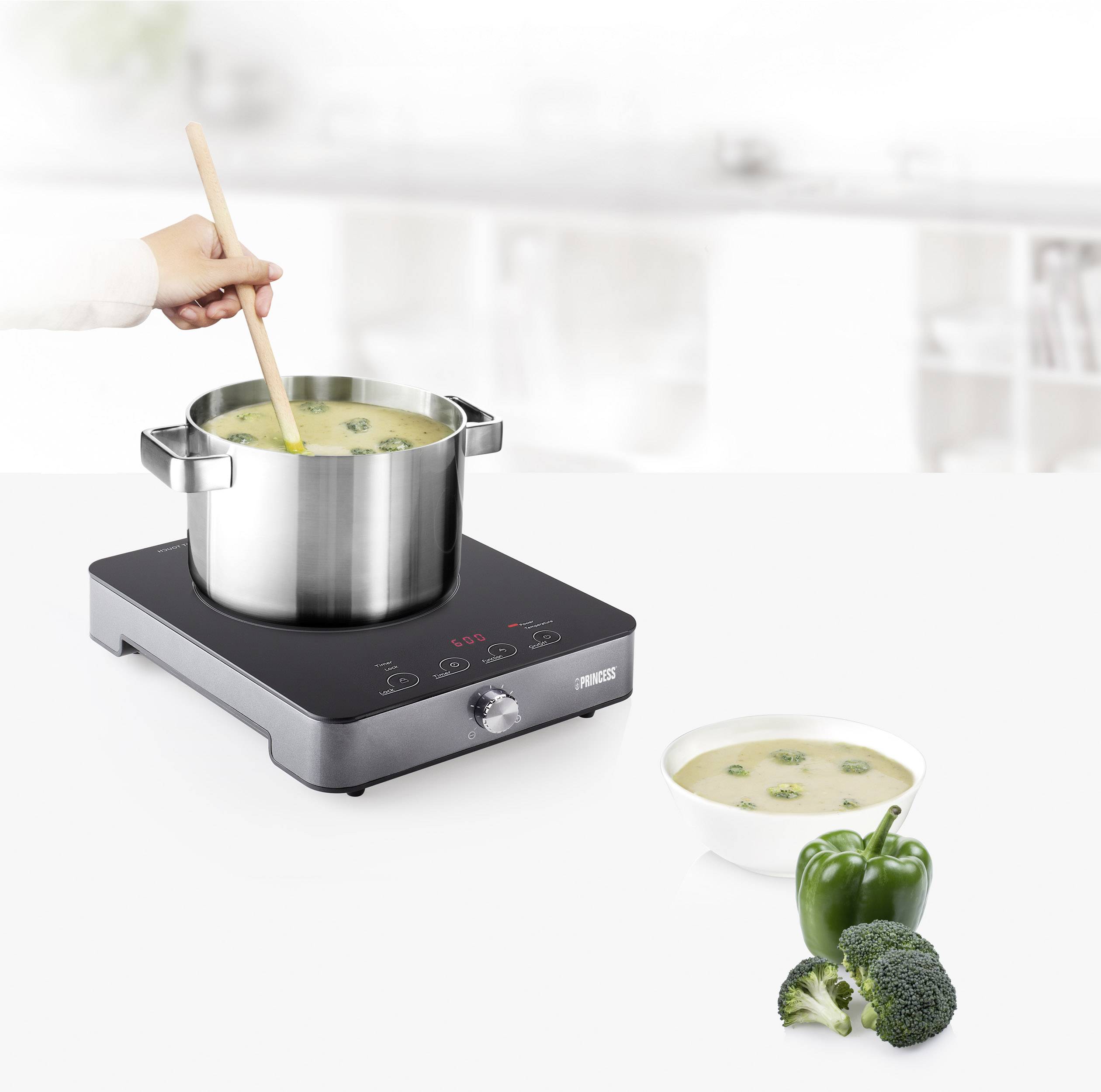 Una mano sta mescolando una pentola di zuppa su un fornello. Accanto, c'è una ciotola di zuppa con broccoli e un peperone verde.