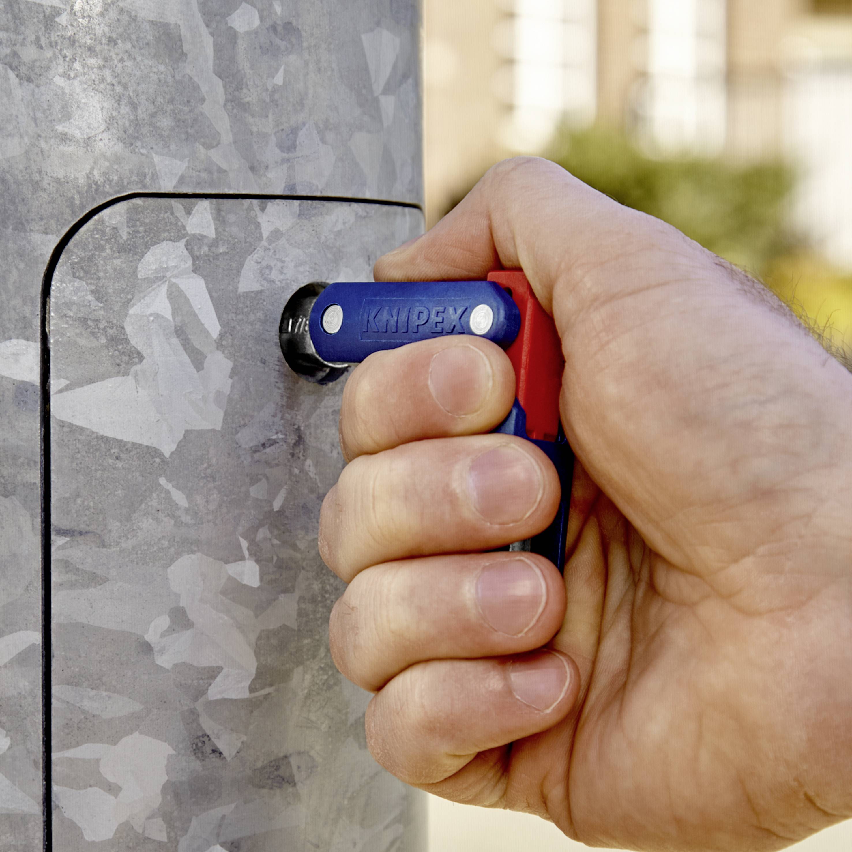 Una mano tiene una chiave regolabile Knipex e sta ruotando il lucchetto di un coperchio metallico di un quadro elettrico.