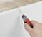 Una mano impugna un cacciavite che graffia la superficie di una lastra di polistirolo bianco.