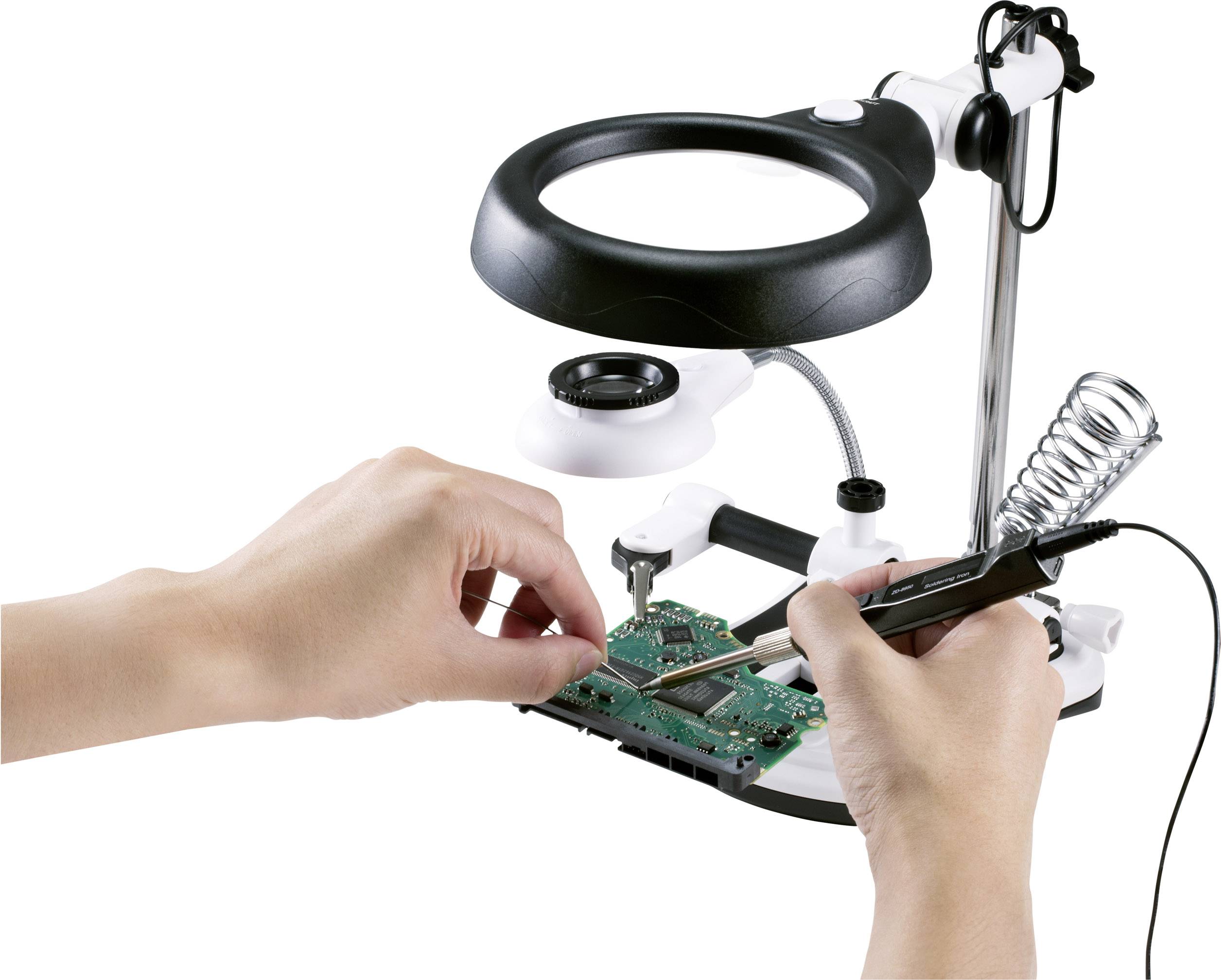 Una persona salda circuiti elettronici su un tavolo da lavoro con una lente di ingrandimento e un saldatore.