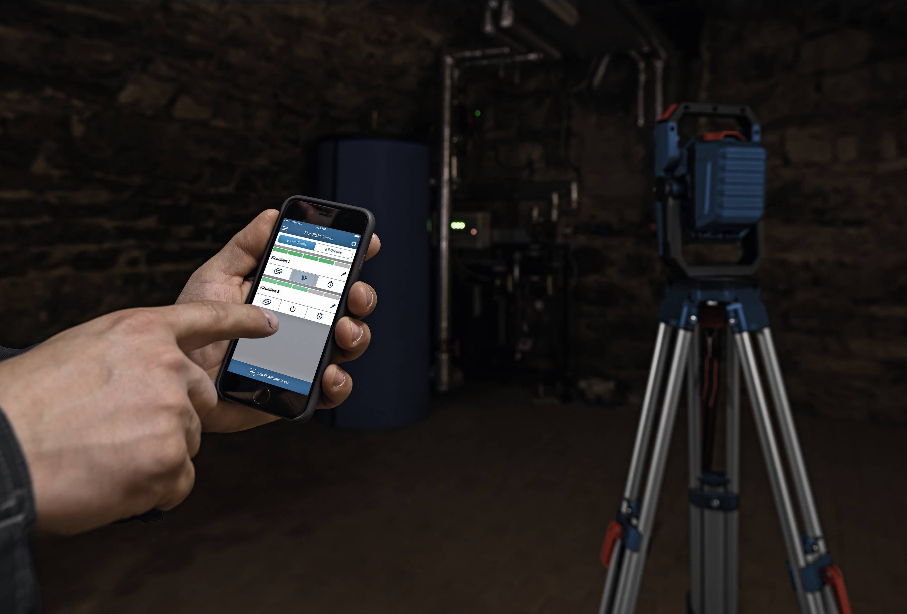 Una persona sta utilizzando un'app su uno smartphone per controllare un dispositivo montato su un treppiede in un ambiente industriale.