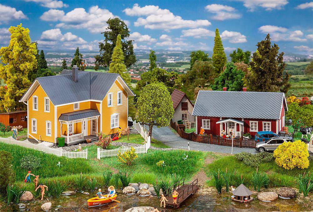 Un paesaggio in miniatura mostra due case colorate, alberi e figure vicino a uno stagno. Persone nuotano e fanno giri in barca, sotto un sole splendente.