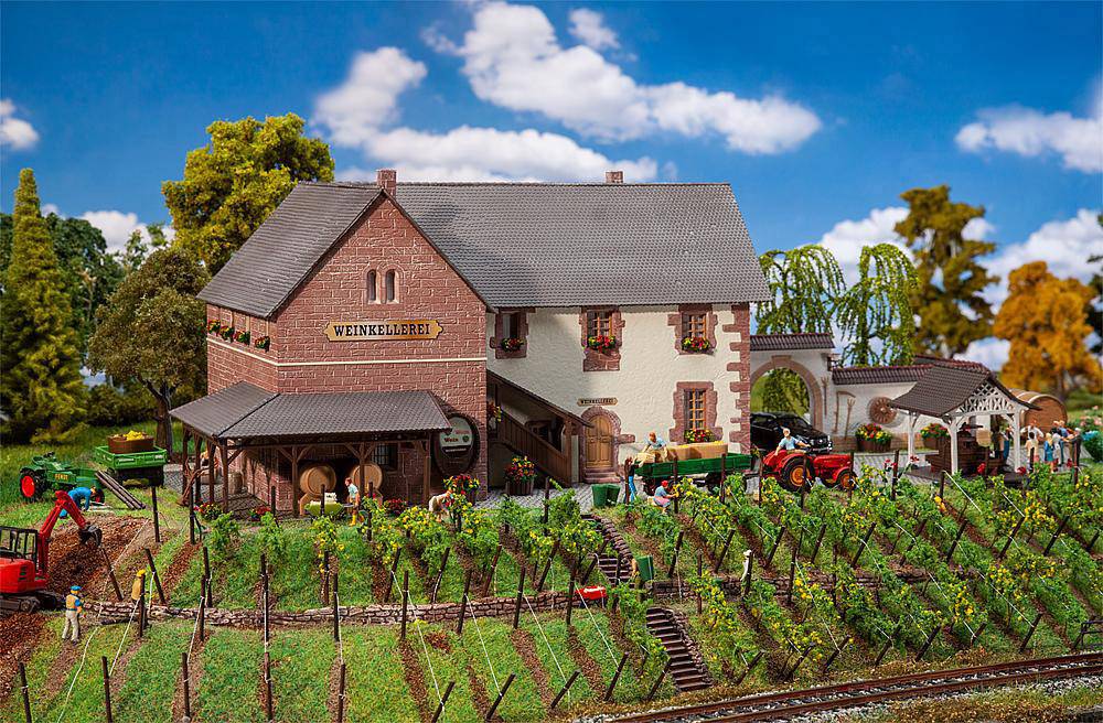 Un modellino in miniatura mostra una cantina con vigneti e trattori sotto un cielo blu con nuvole bianche.