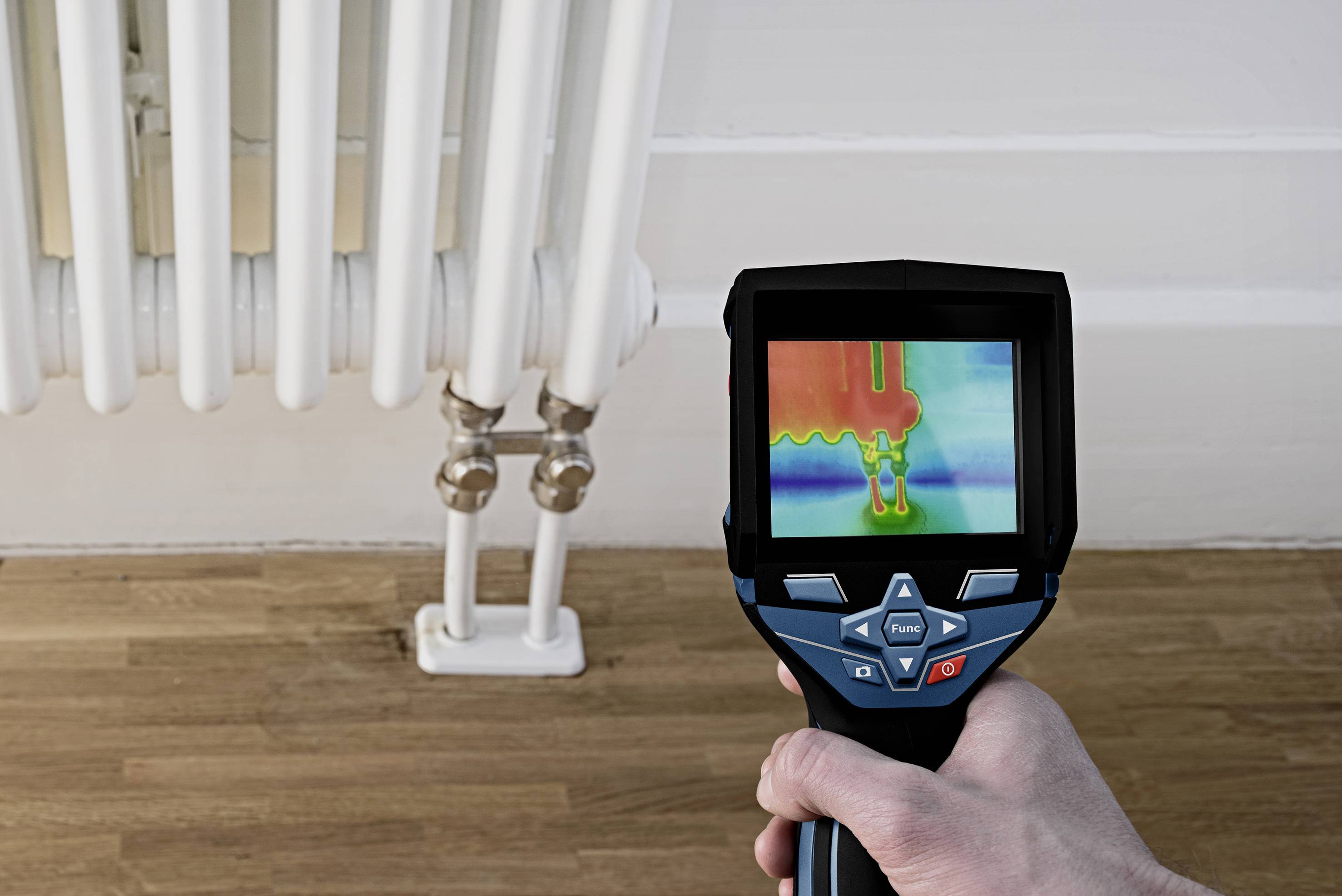 Una mano tiene una termocamera che inquadra un radiatore. Lo schermo mostra le differenze di temperatura dei tubi del riscaldamento.