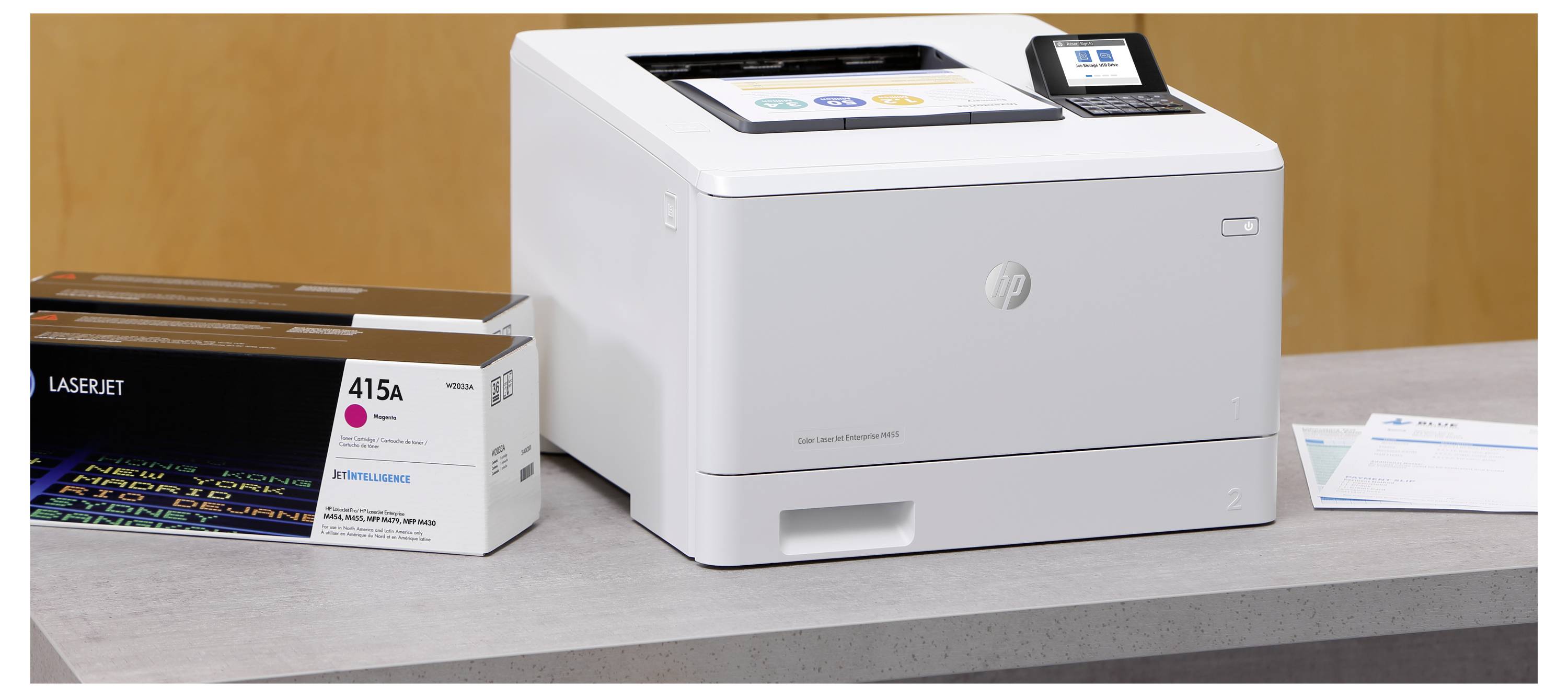 Una stampante HP LaserJet su una scrivania accanto a una scatola di cartucce di toner 415A, con una piccola pila di fogli vicino.