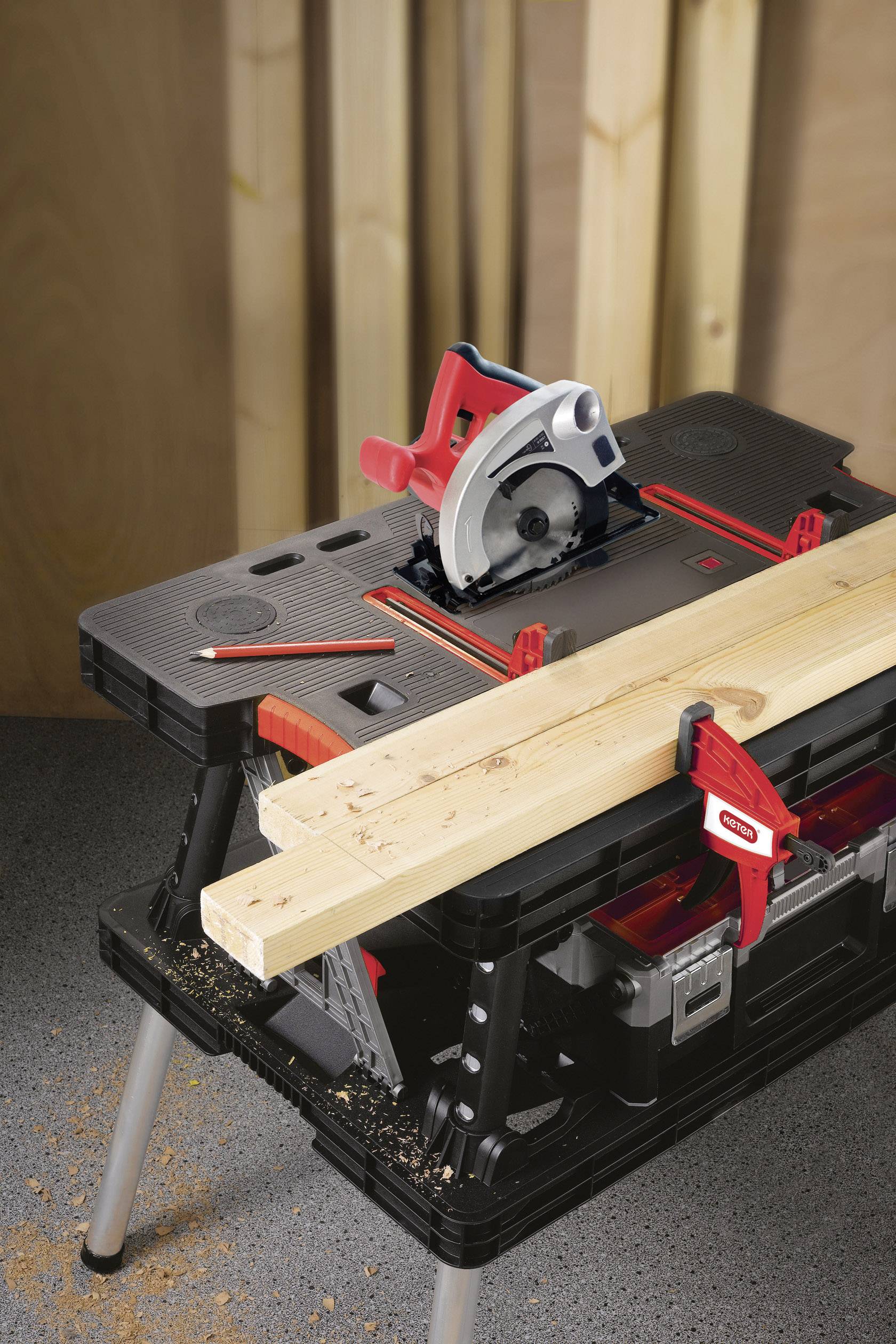 Una sega circolare da banco su un cavalletto sta tagliando due travi di legno. Sullo sfondo si vedono tavole di legno verticali.