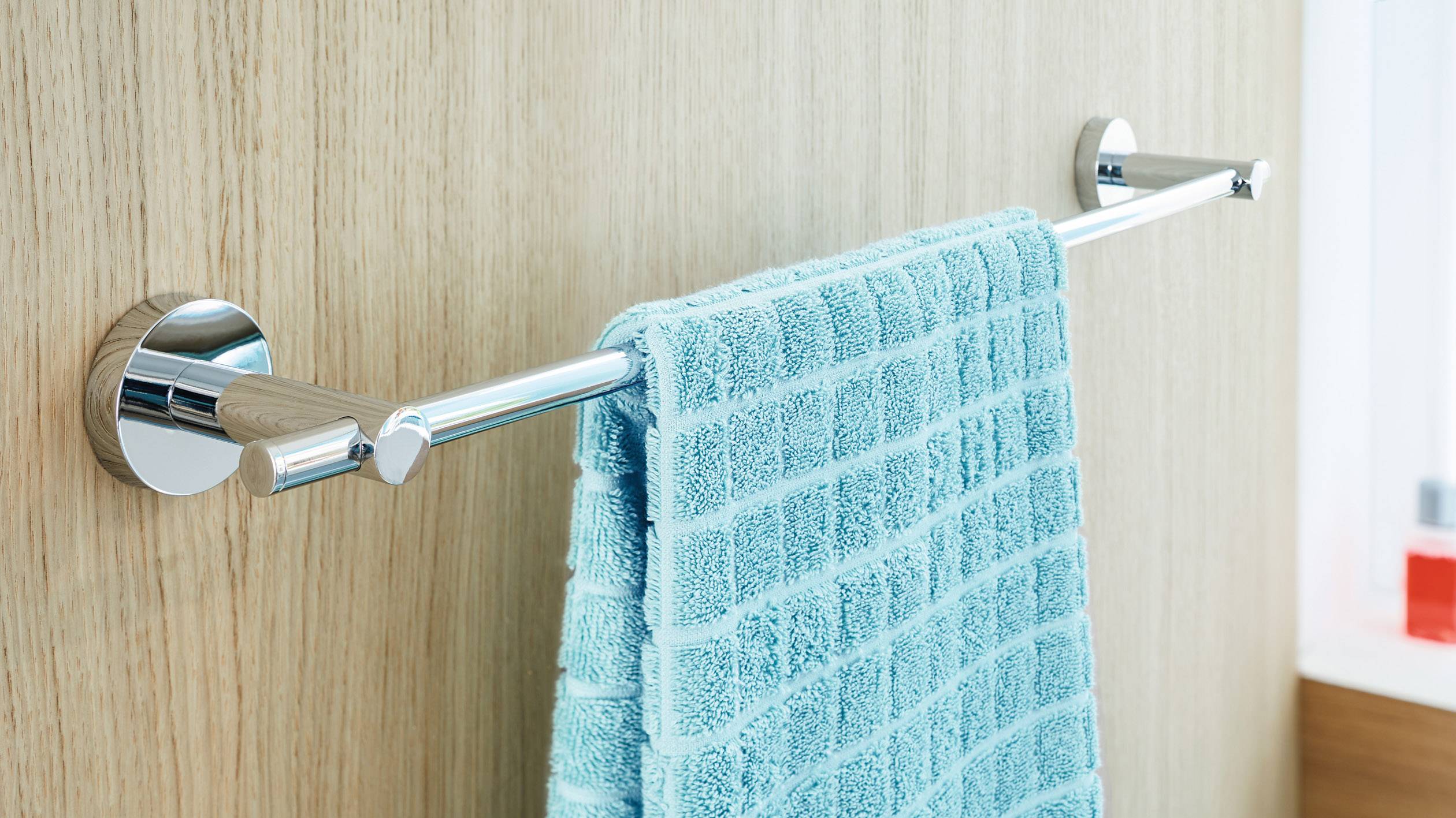 Un asciugamano color turchese è appeso a un portasciugamani lucido su una parete di legno in un bagno.