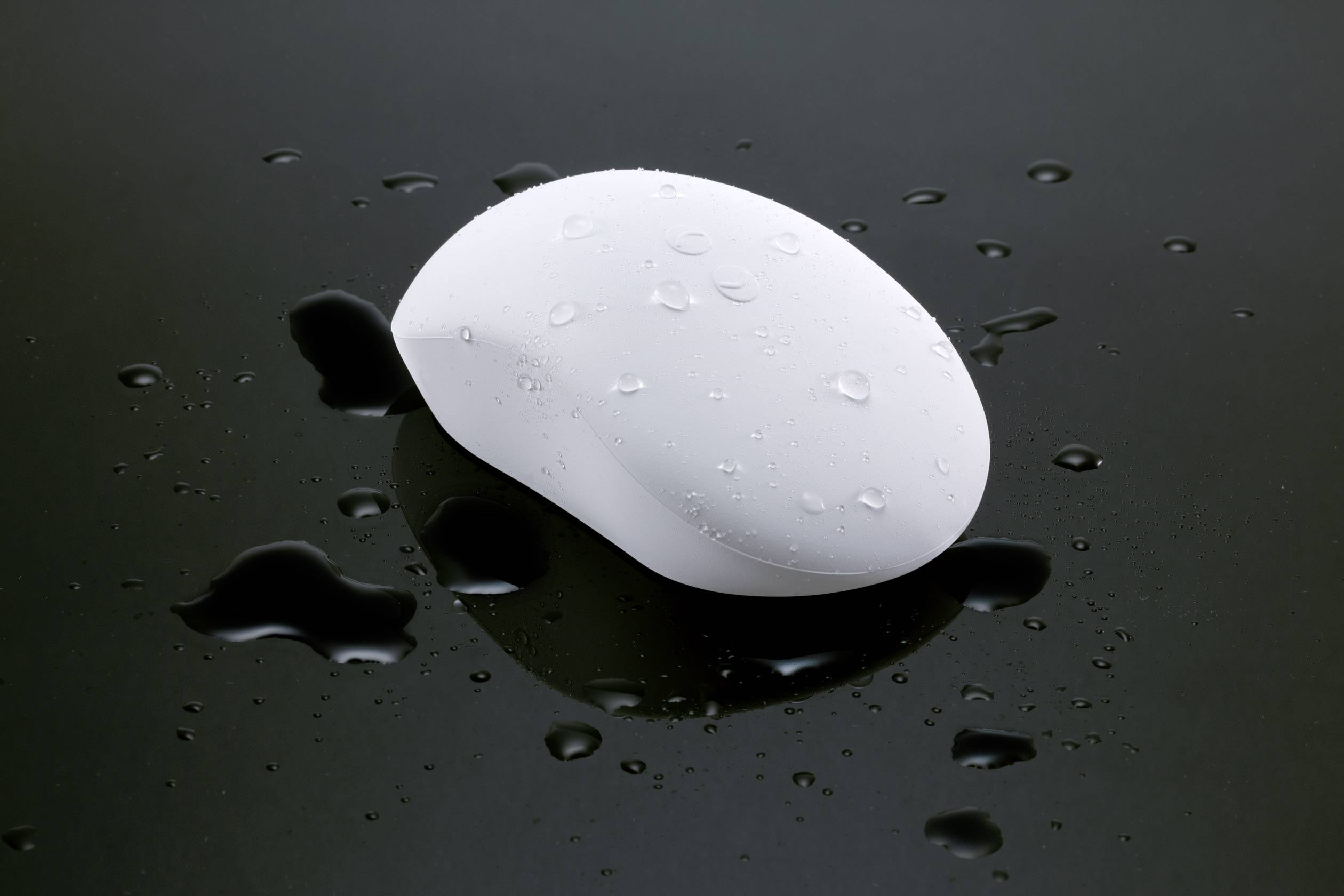 Un mouse wireless bianco su sfondo nero, cosparso di gocce d'acqua, che suggerisce umidità o bagnato.