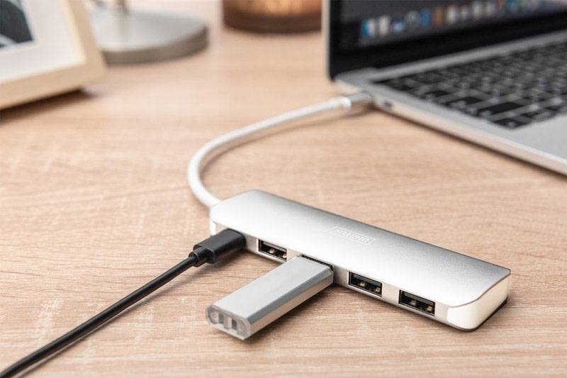 Un laptop è collegato tramite un hub USB-C a diverse chiavette USB che sono posizionate su un tavolo di legno.
