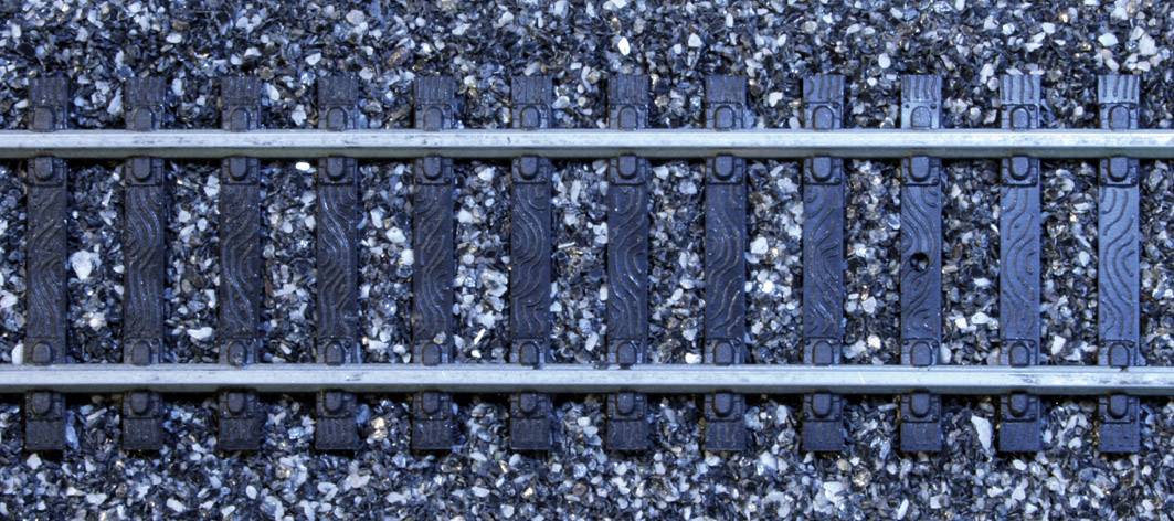 Binari di un modello ferroviario su un letto di ghiaia grigia, allineati simmetricamente.