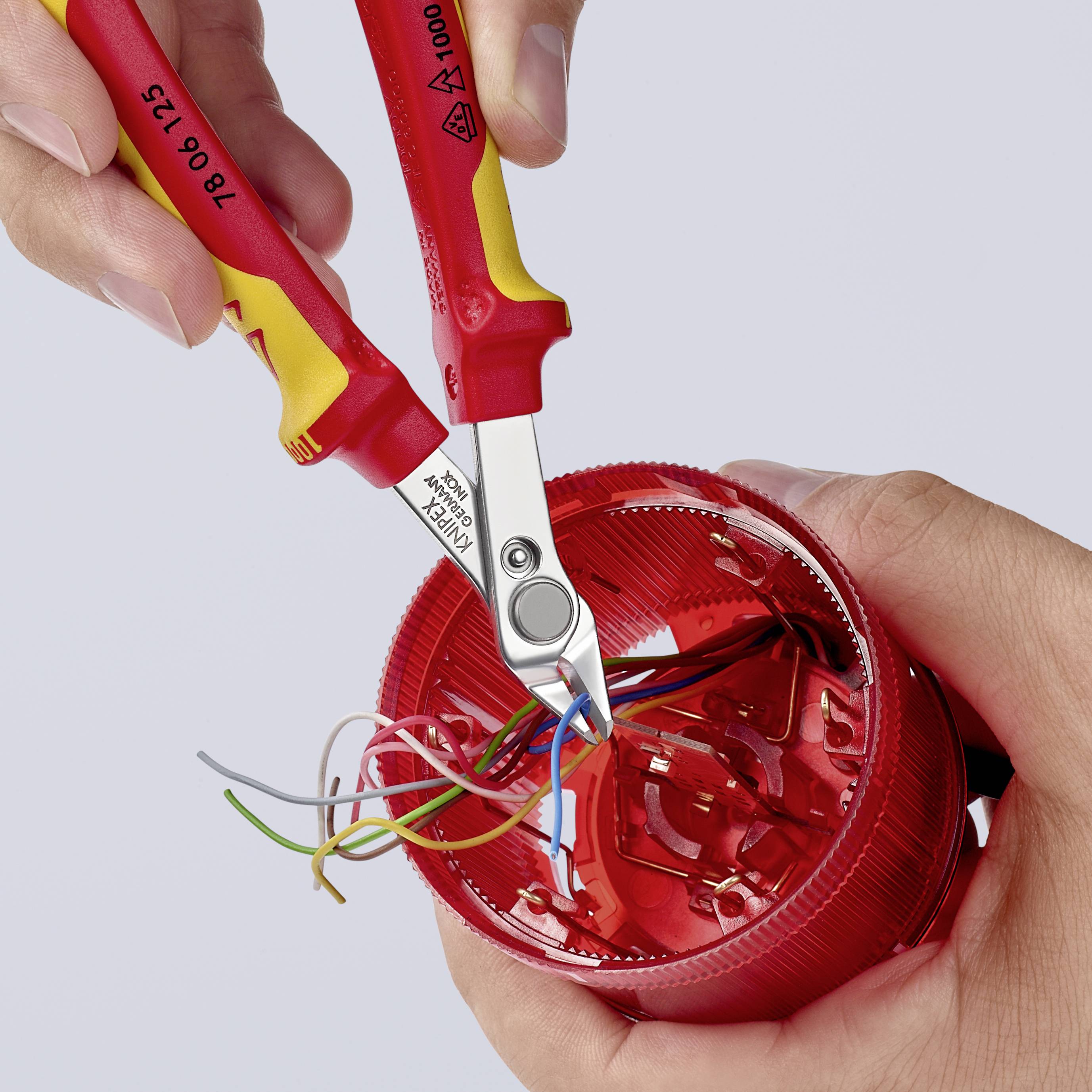 Due mani utilizzano un tronchese per rimuovere cavi colorati da una parte rotonda rossa in plastica.