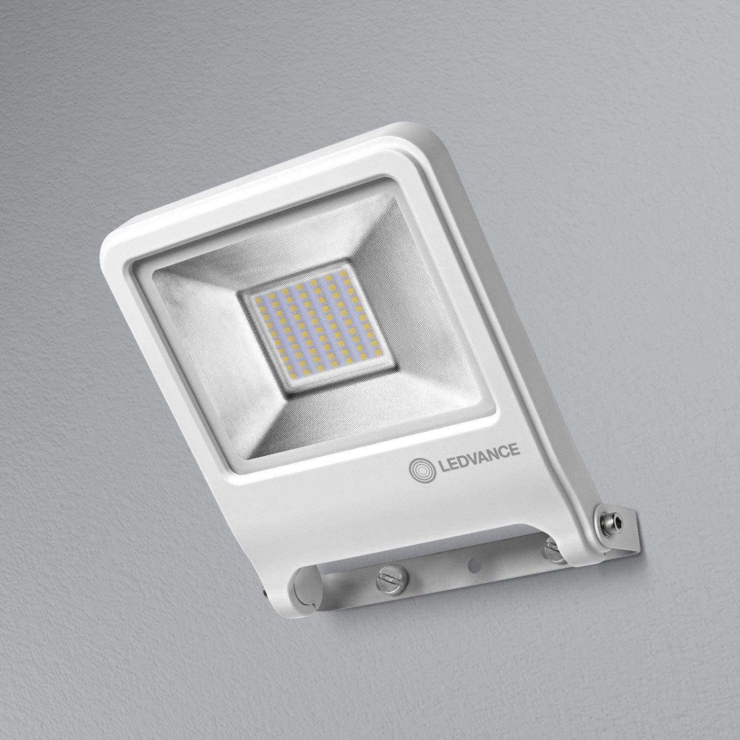 Un proiettore LED quadrato con cornice bianca montato su una parete grigia. Il pannello LED è composto da diversi piccoli diodi.