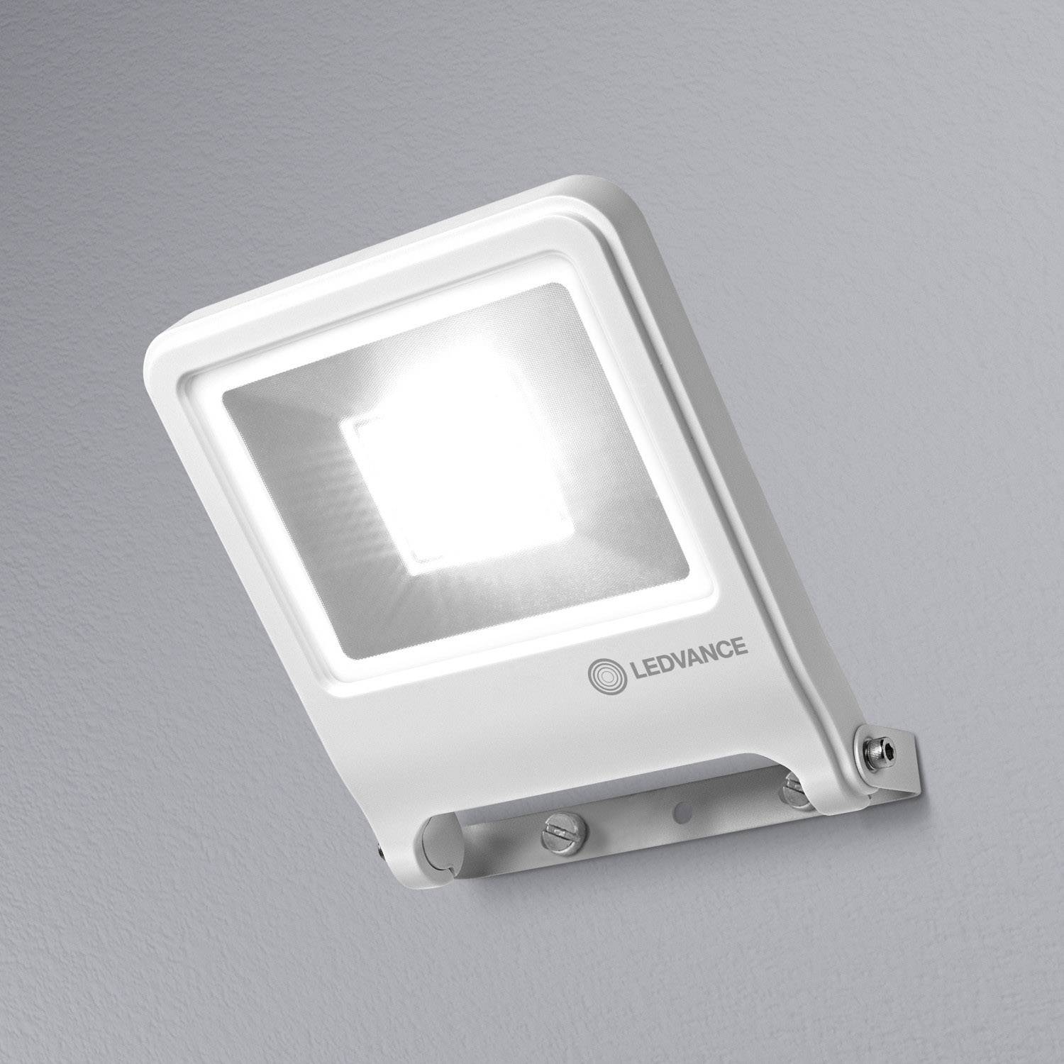 Una lampada LED esterna bianca è montata su una parete grigia. Emana una luce intensa e porta il logo 'LEDVANCE'.