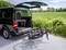 Un bagagliaio aperto di un furgone con un portabiciclette estraibile, due biciclette montate, campi verdi sullo sfondo.