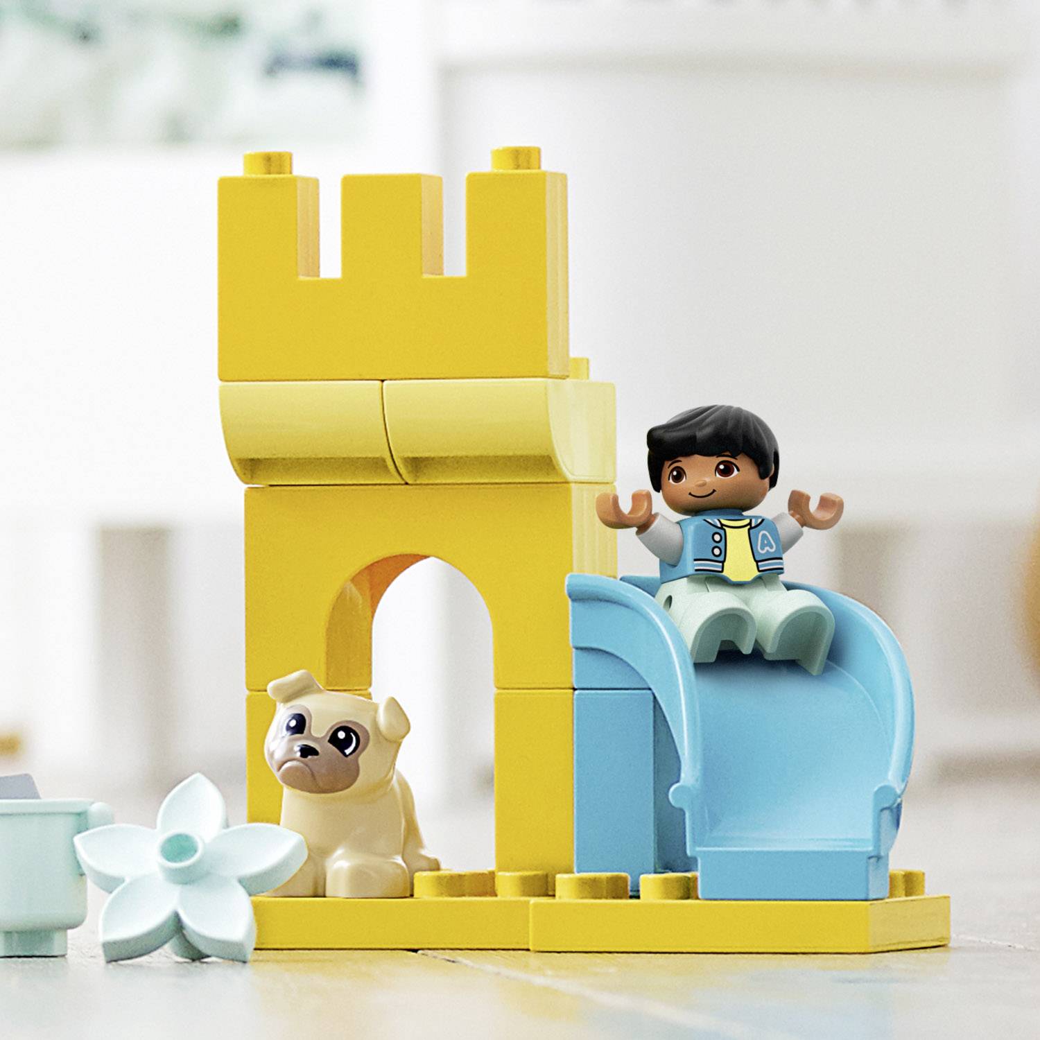 Un giocattolo per bambini con blocchi gialli mostra una torre con uno scivolo. Accanto, una figurina è seduta vicino a un cane.