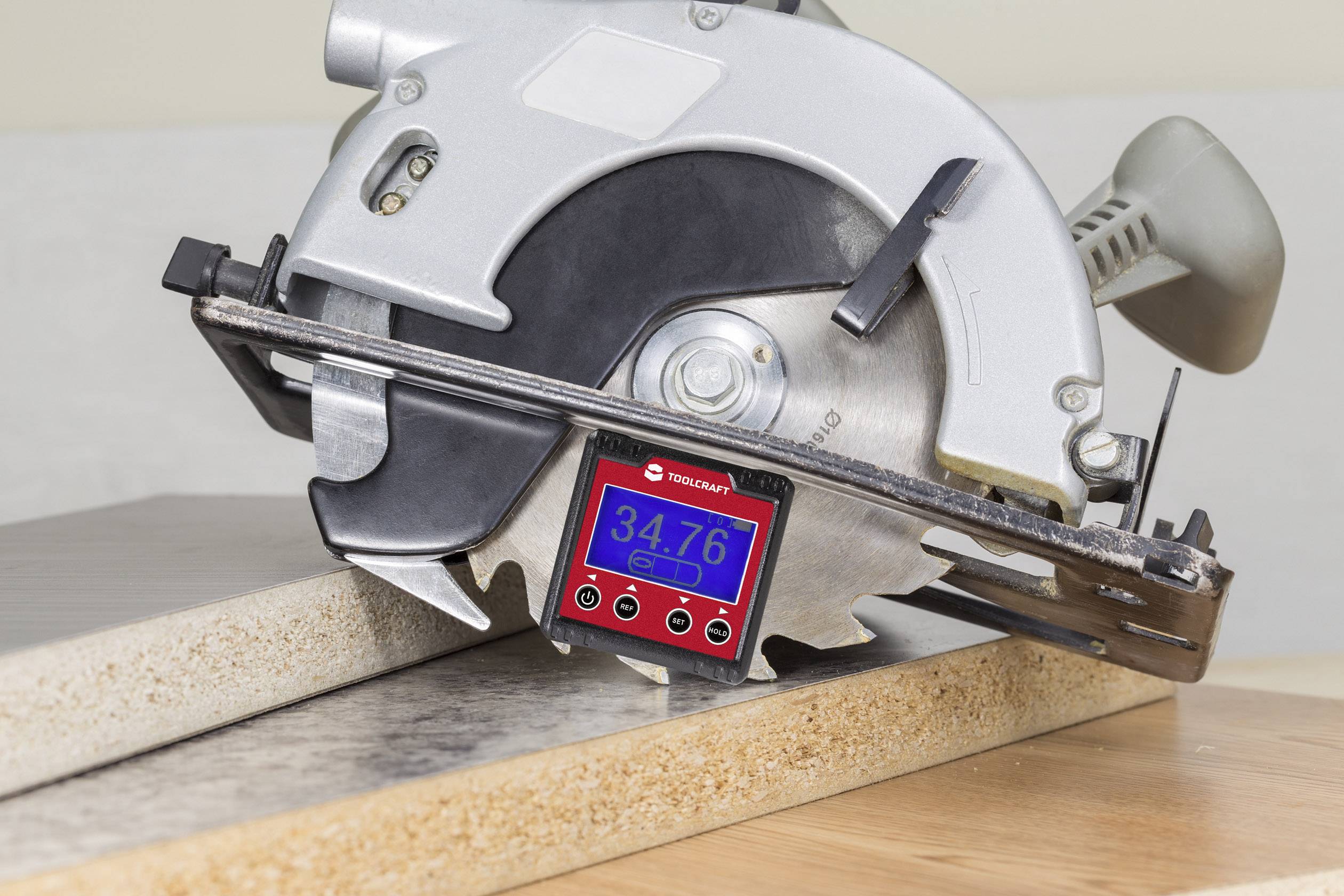 Sega circolare manuale taglia una tavola di legno. Un goniometro digitale è posizionato tra la lama e il legno e mostra '34,76°'.