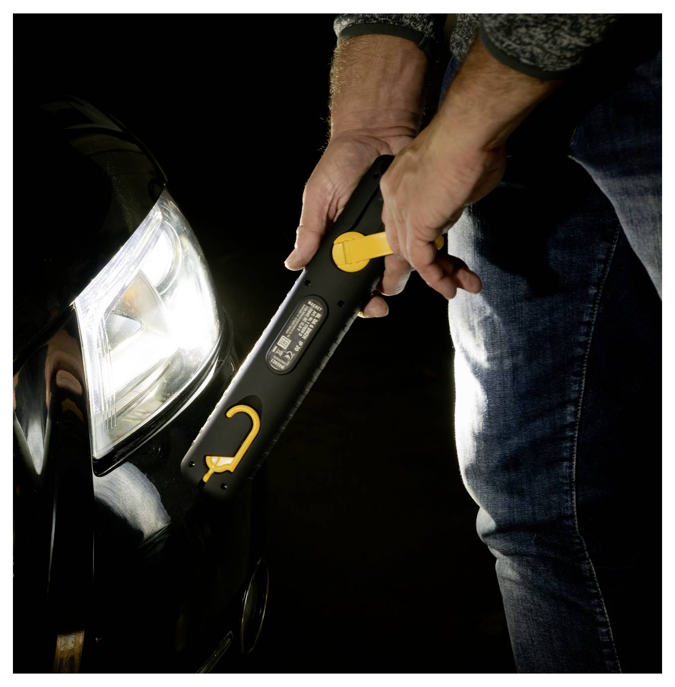 Una persona che utilizza un avviatore portatile su una batteria dell'auto vicino al faro anteriore in un'ambientazione buia.