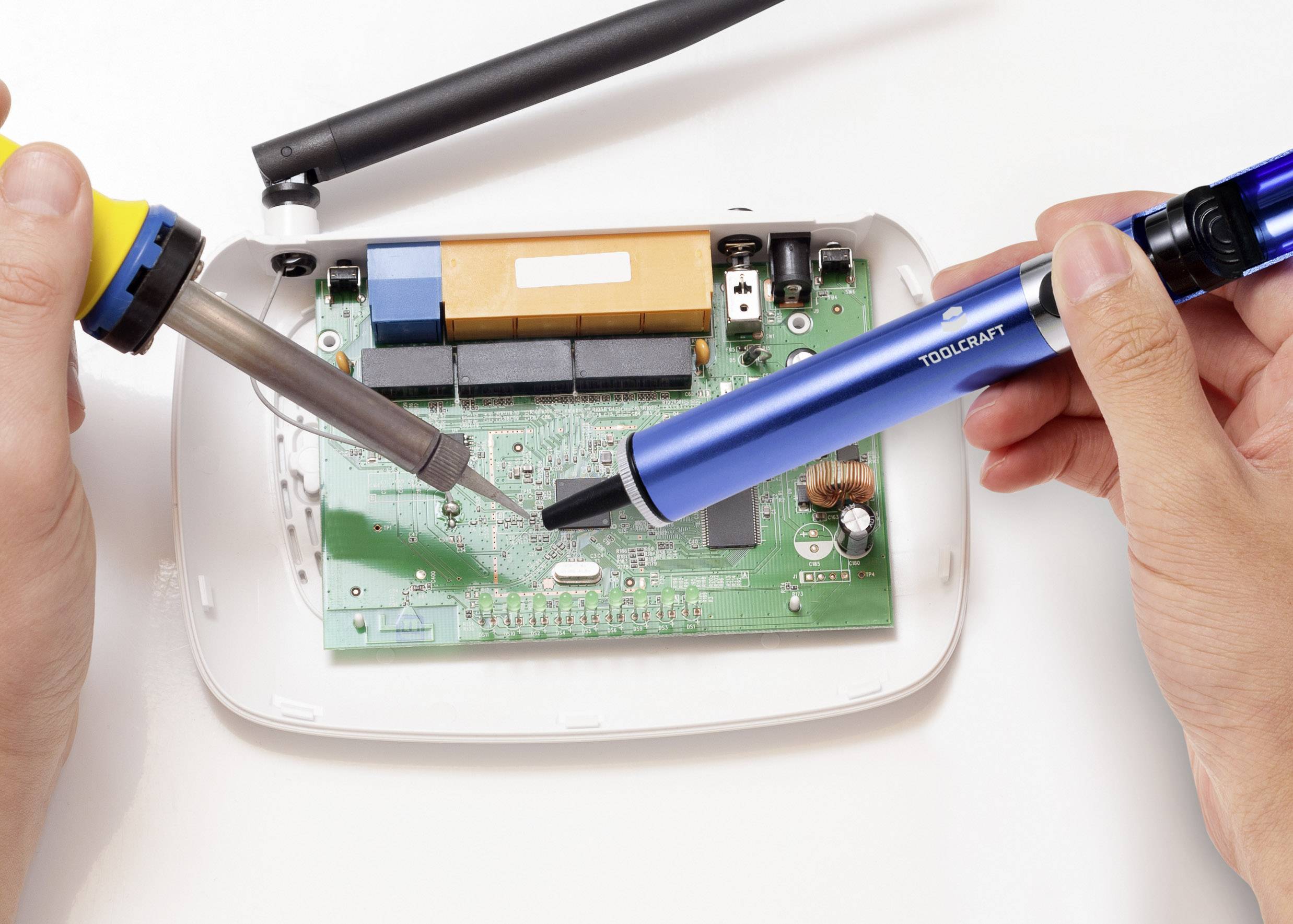 Una persona rimuove componenti da una scheda elettronica utilizzando un saldatore e una pompa dissaldante. L'immagine mostra il processo di riparazione di un dispositivo elettronico.