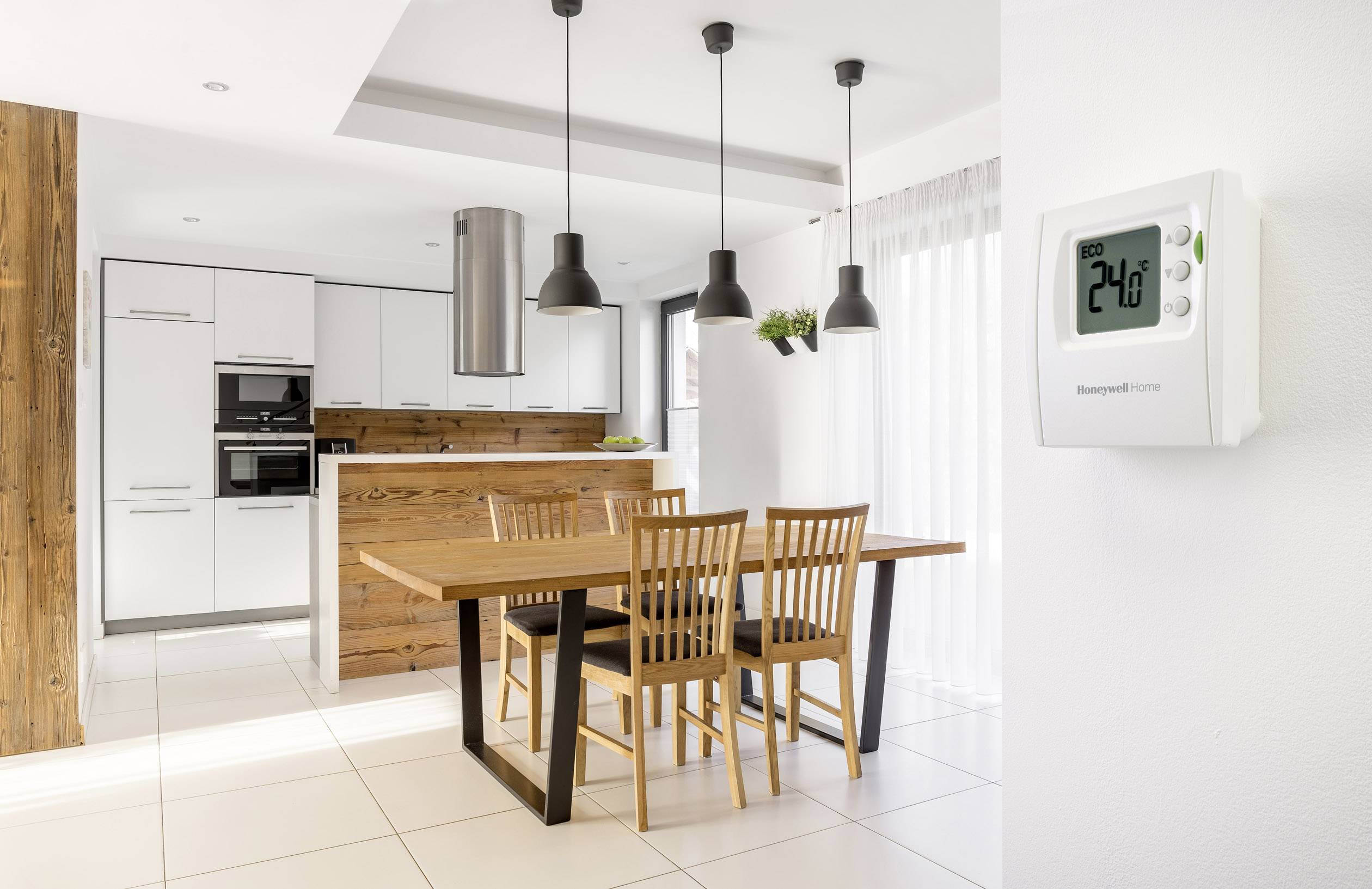 Soggiorno luminoso e moderno con tavolo da pranzo e sedie, adiacente a una cucina open space. Sulla parete è appeso un termostato che indica 24°C.