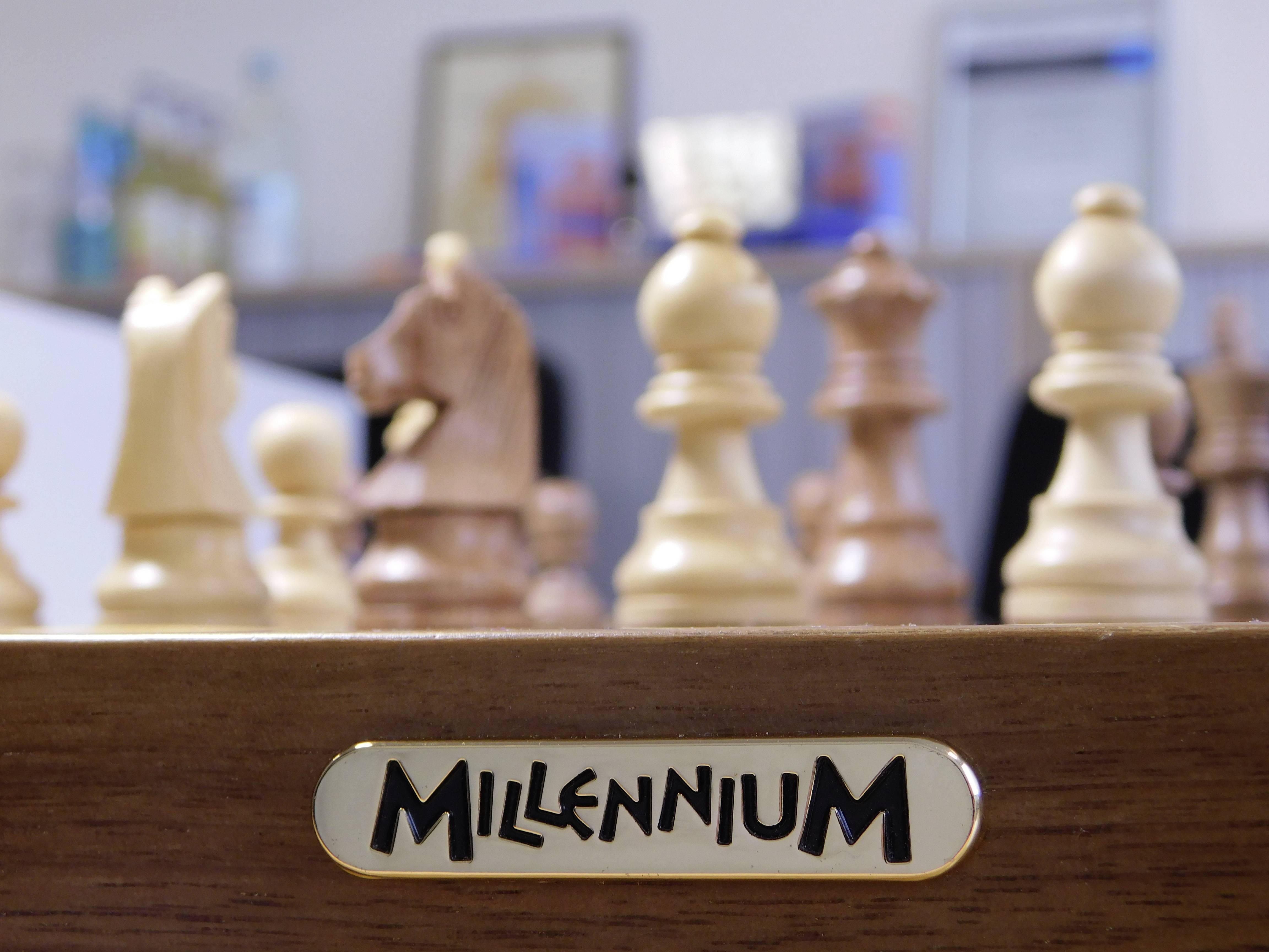 Una serie di pezzi degli scacchi su una scacchiera, con un cartello in primo piano che riporta la scritta 'Millennium'.