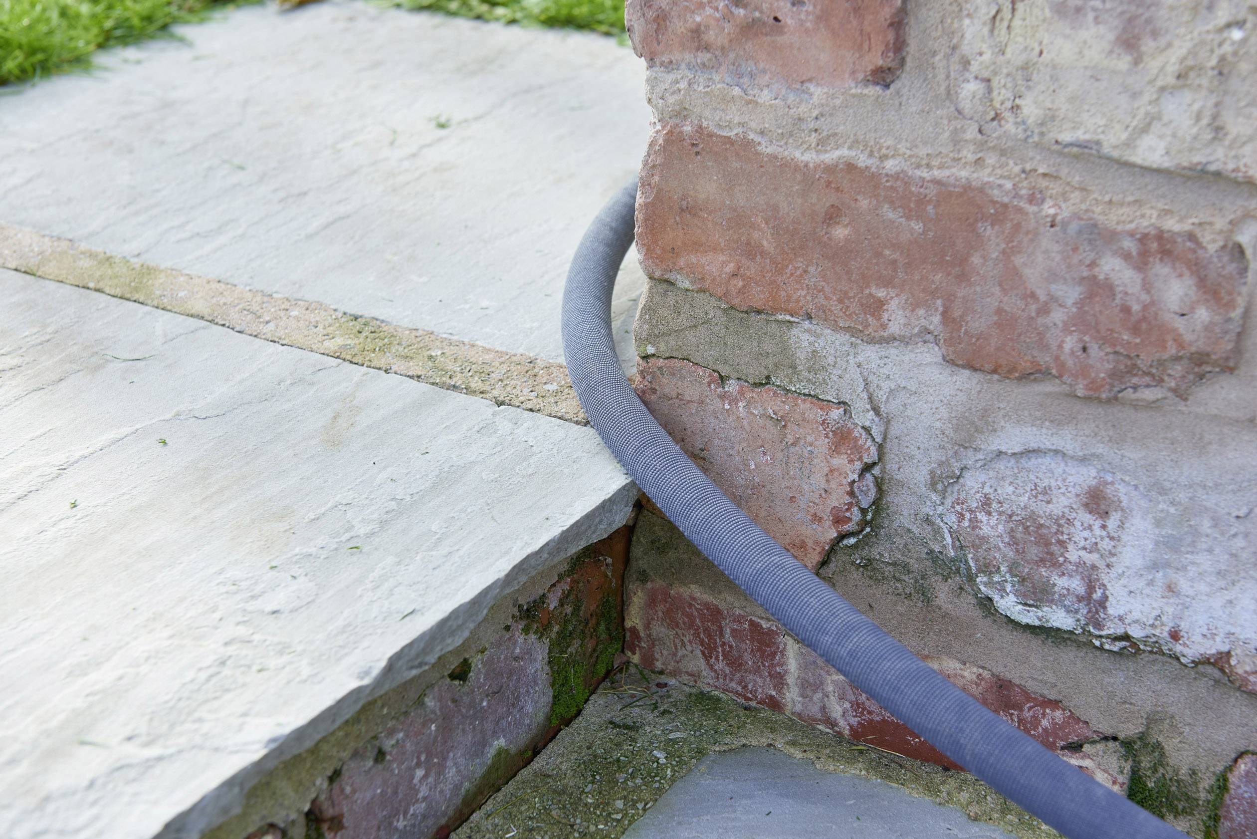Un tubo grigio si estende sopra un gradino di pietra lungo un muro di mattoni all'aperto.