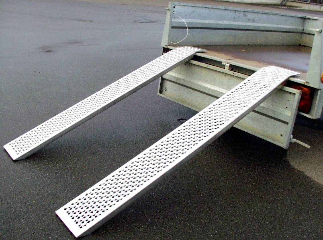Rampe metalliche fissate a un rimorchio, su una superficie di asfalto bagnato, consentono un carico e scarico agevole.