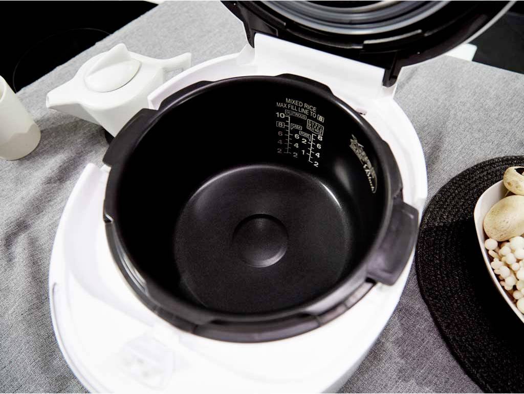 Un rice cooker aperto su un tavolo con un panno grigio; accanto c'è un piatto con funghi e un cestino.