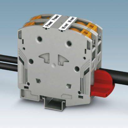 Connettore elettrico grigio con cavi neri inseriti sul lato. Sulla parte superiore sono presenti etichette con testo.
