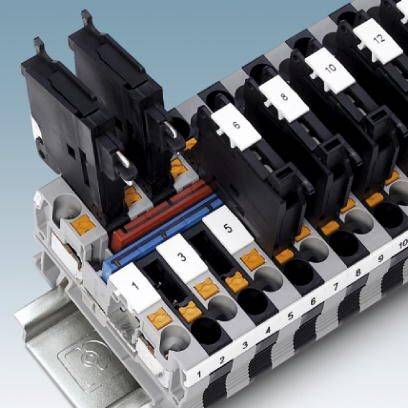 Blocco morsetti di connessione con più attacchi di corrente numerati, realizzato in plastica e metallo, montato su una guida.
