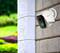 Una telecamera di sorveglianza è montata su un muro di mattoni, sorvegliando un giardino verde sullo sfondo.