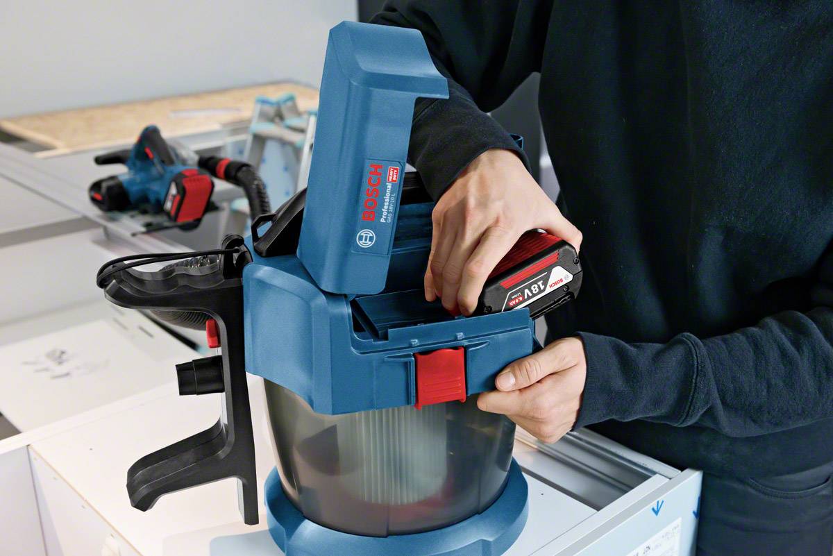 Una persona sta cambiando la batteria di un aspirapolvere blu Bosch in un laboratorio.