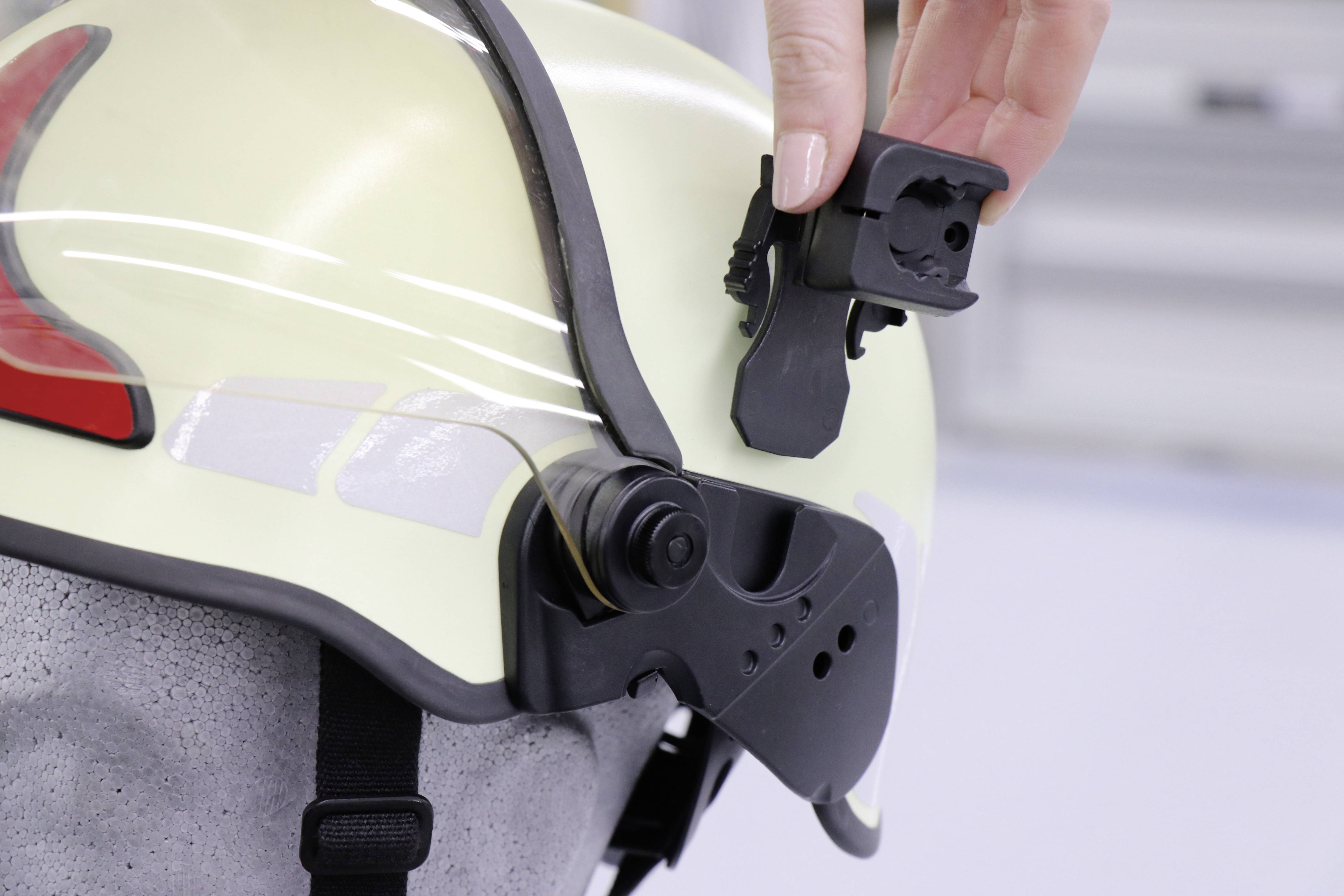 Una mano posiziona un supporto per accessori su un casco giallo con fissaggio nero.